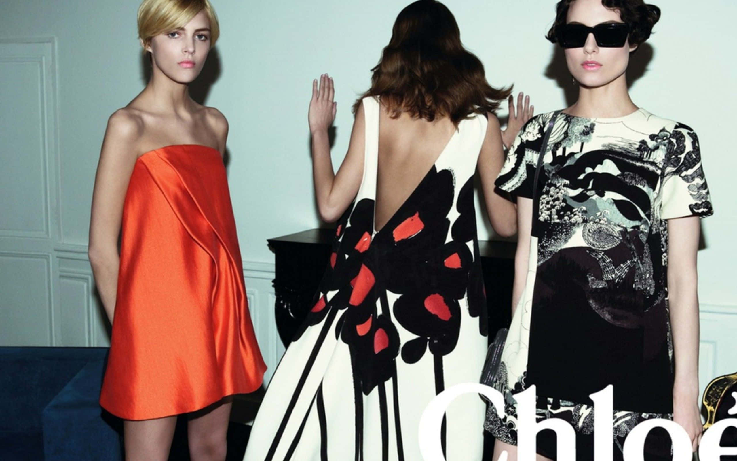 Spring Fashion 桌布 壁紙 — 三位模特兒穿著大膽時尚的連衣裙，在簡約的白色牆壁和藍色地毯前擺姿勢。
