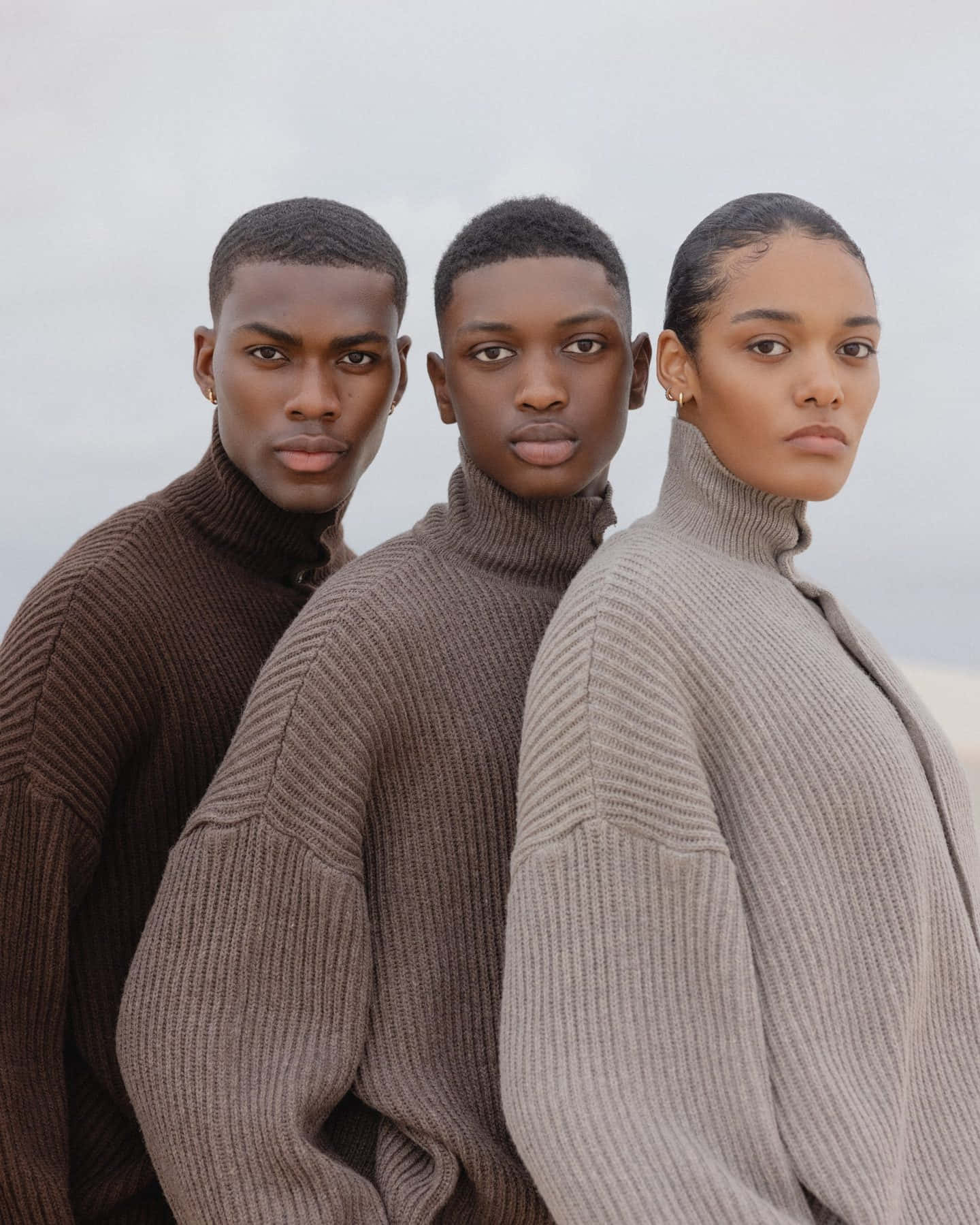 Minimalist Fashion 桌布 壁紙 — 三位模特兒穿著羅紋高領毛衣，排成一排，背景是柔和天空，直視鏡頭，表情嚴肅。
