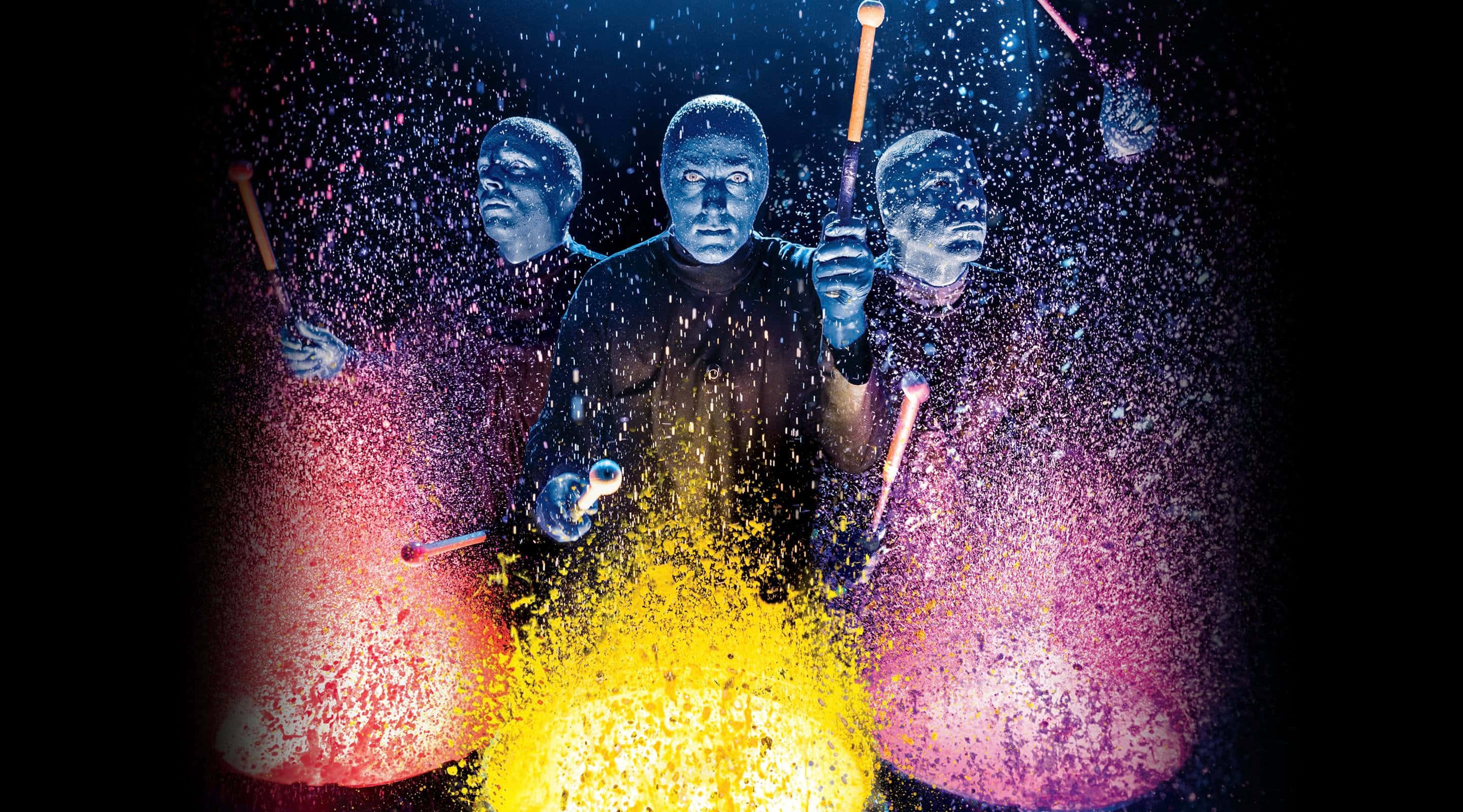 Blue Man Group 桌布 壁紙 — 三位藍面鼓手在黑暗舞台上，於戲劇性燈光下爆發出鮮豔的彩色火花。