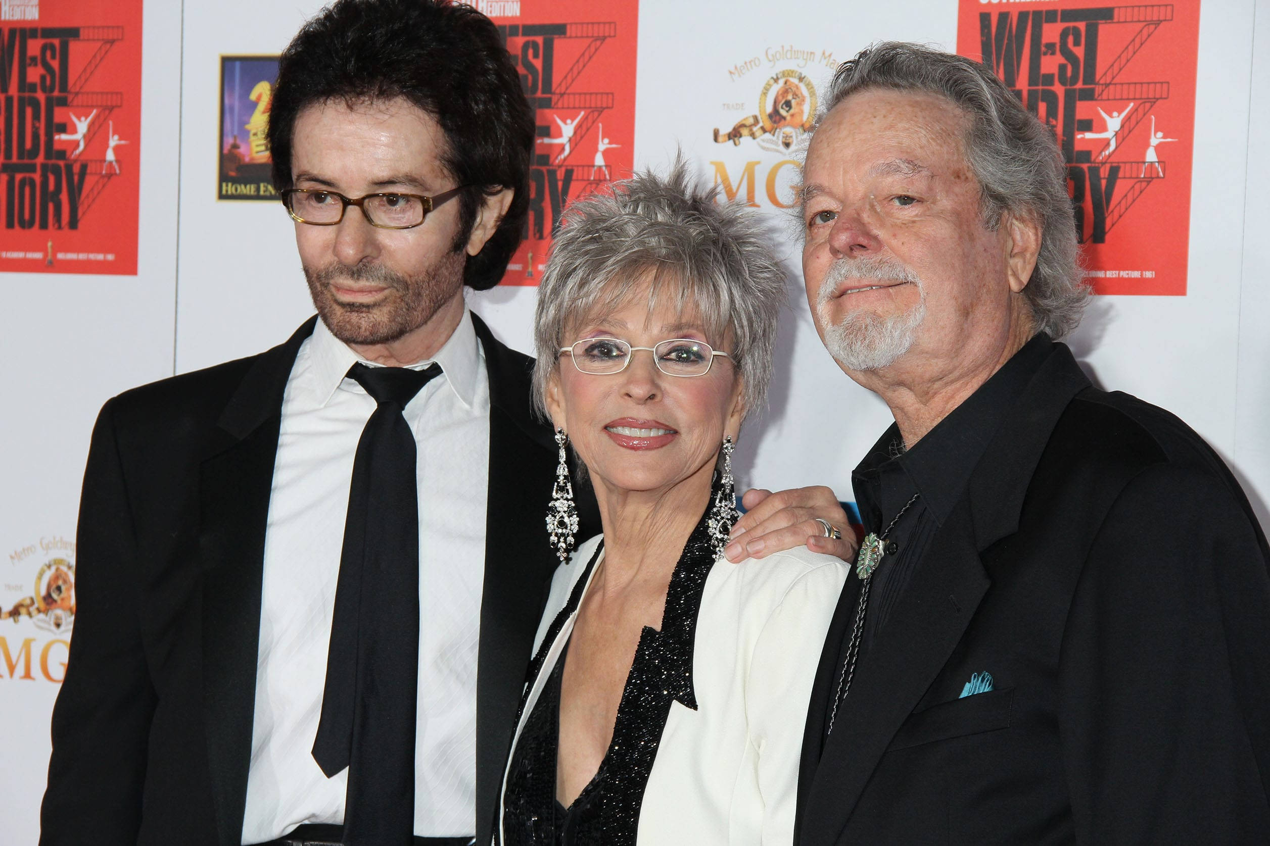 George Chakiris、Rita Moreno、Russ Tamblyn 壁紙 — 三位衣著優雅的名人一起在紅地毯活動上擺姿勢，背後有宣傳橫幅。