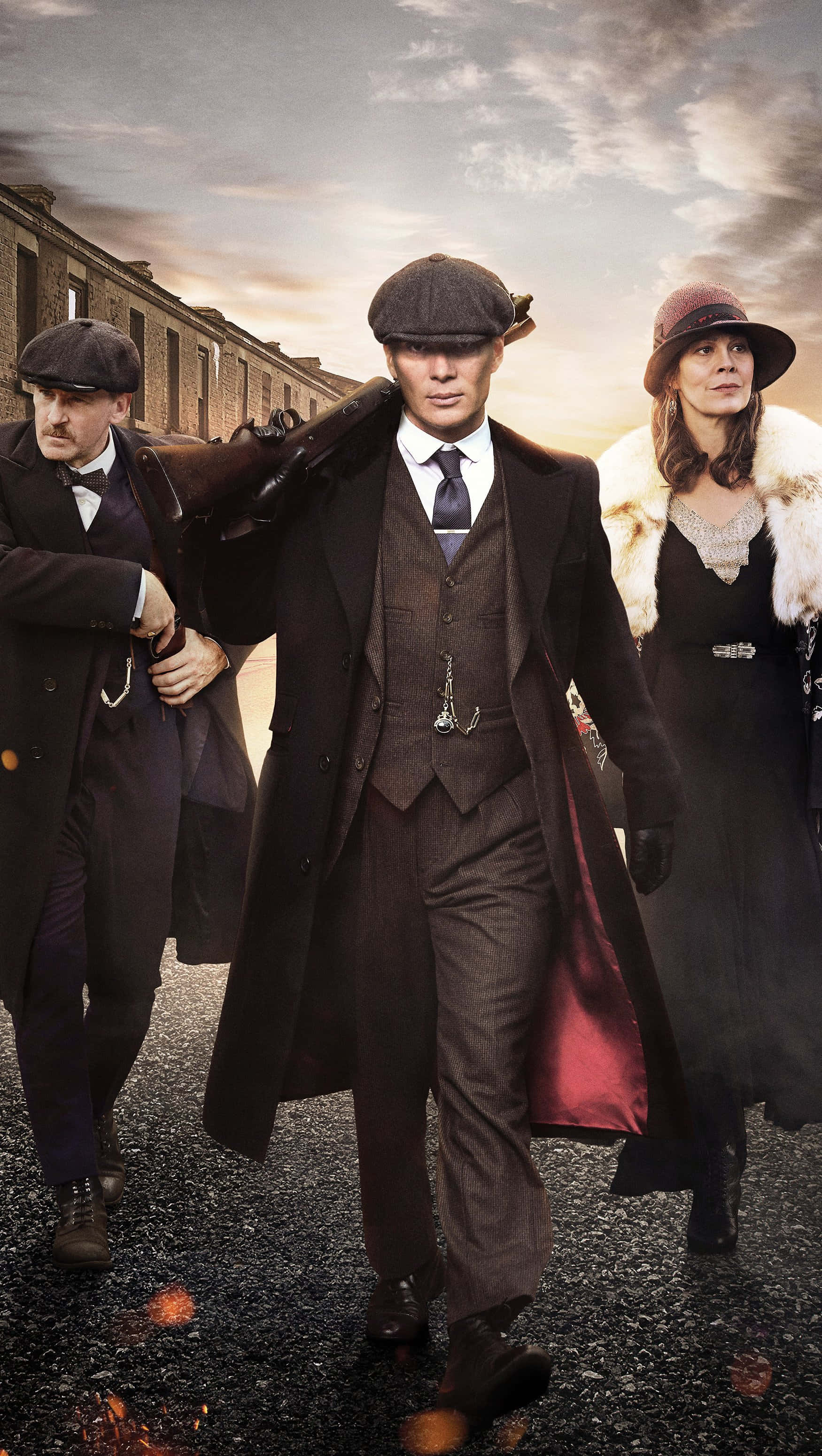 Peaky Blinders 桌布 壁紙 — 三位衣著時尚的1920年代黑幫份子，在陰沉的暮色天空下，大步走過一條粗糙的城市街道。