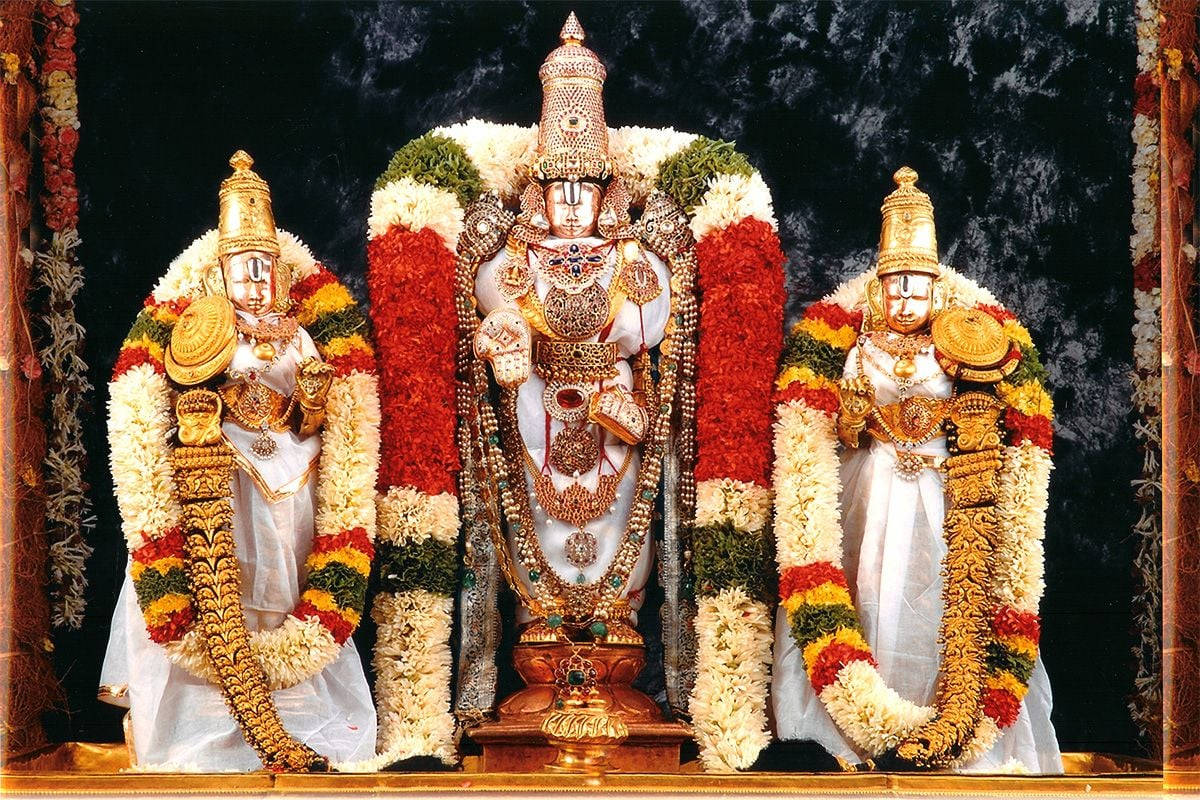 Venkateswara Swamy 桌布 壁紙 — 三位裝飾華麗的印度教神祇，佩戴金飾和鮮豔花環，莊嚴地站在黑暗背景前。