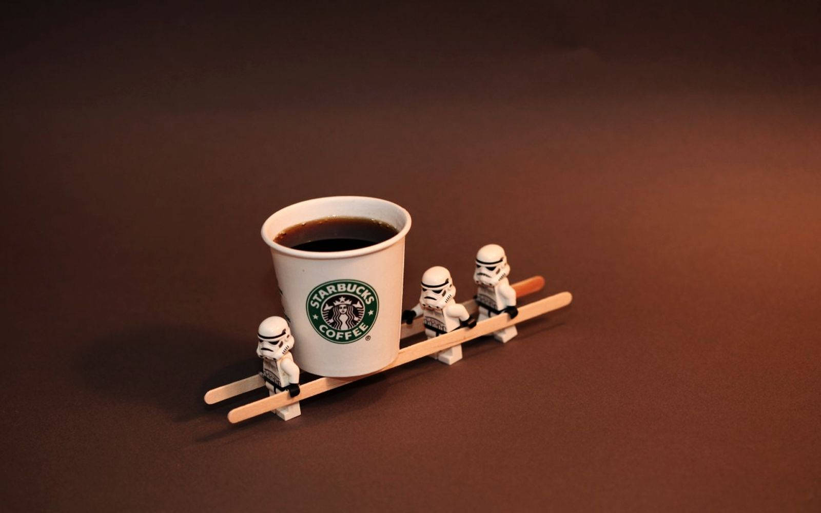 白兵 桌布 壁紙 — 三個 LEGO 白兵在溫暖的棕色背景下用木製雪橇拉著一杯 Starbucks 咖啡杯。