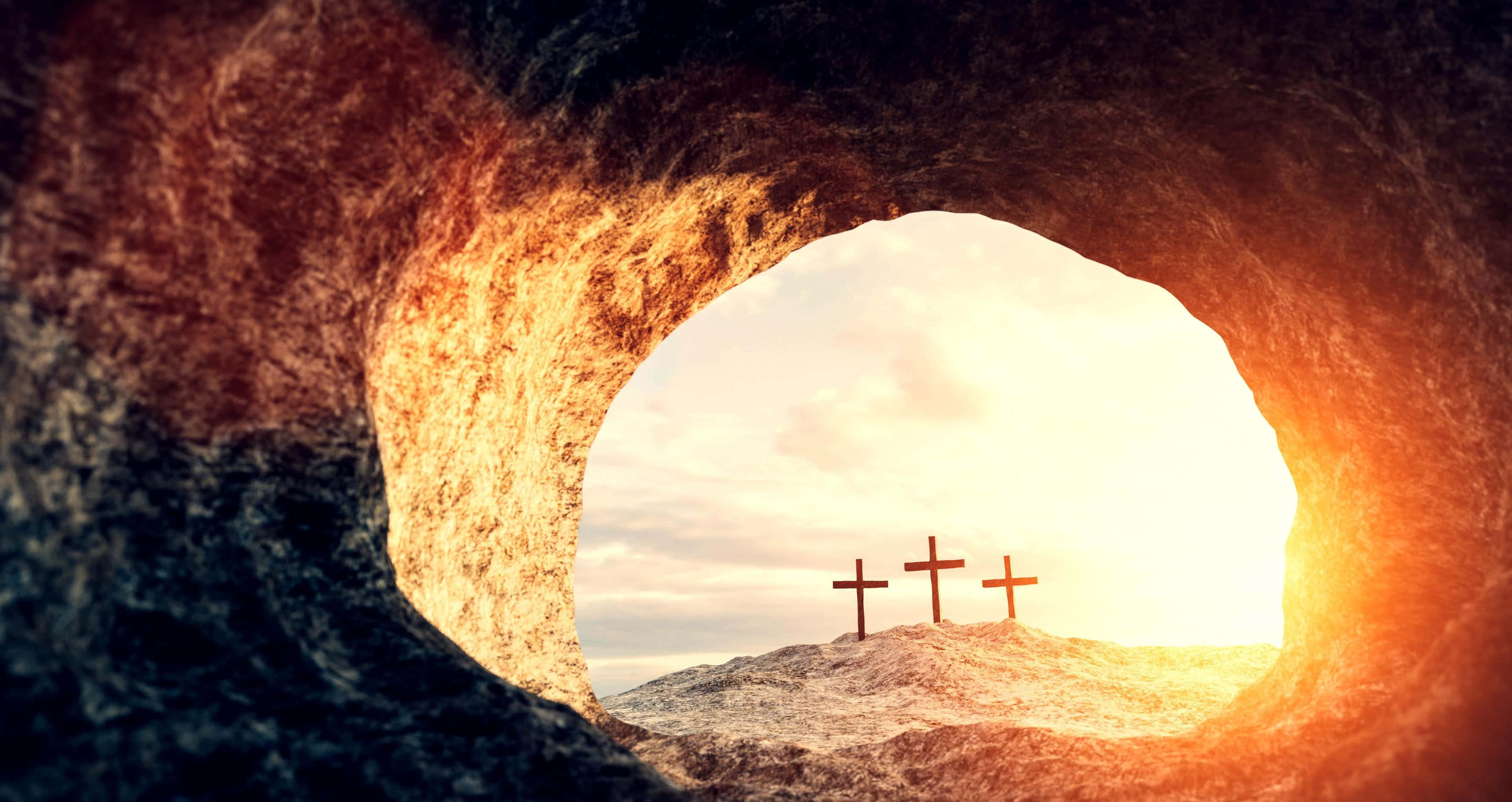 Jesus Resurrection 桌布 壁紙 — 三個十字架矗立在山丘上，沐浴在金色的日出光芒中，透過岩石墓穴的圓形開口觀看。
