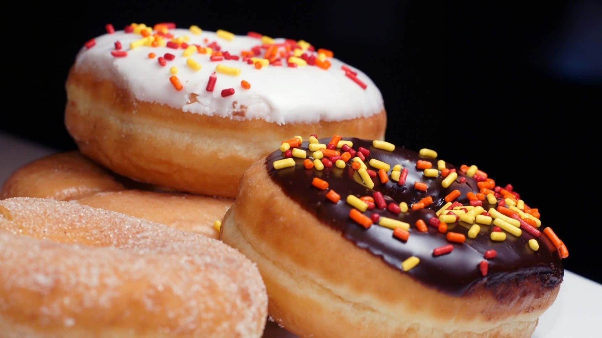 donuts 桌布 壁紙 — 三個帶有彩色糖粒和糖衣的釉面冬甩堆疊在白色碟子上，背景為深色。