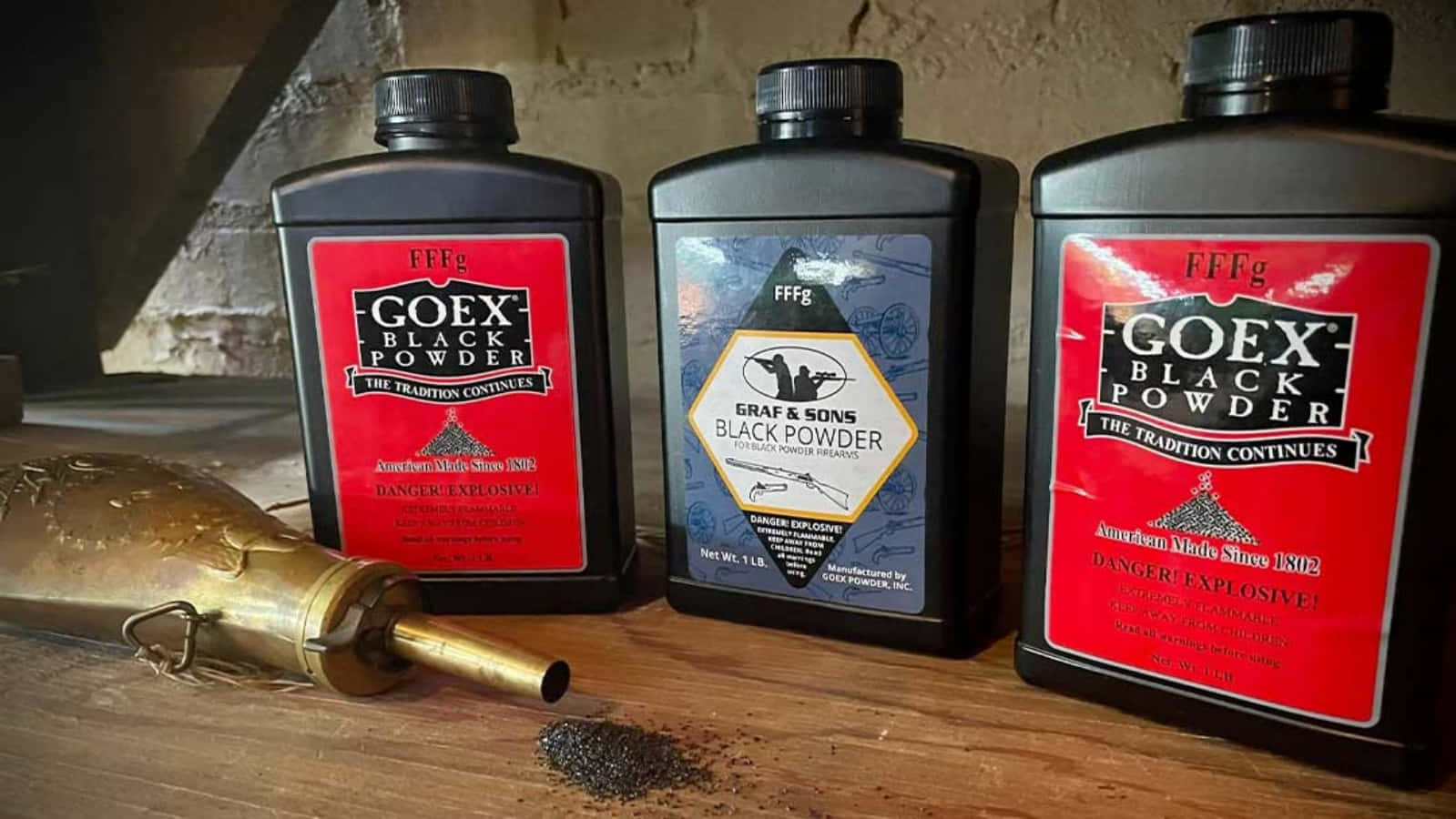 Black Powder 桌布 壁紙 — 三個帶有紅色和藍色標籤的黑色火藥瓶放在木質表面上，旁邊有一個黃銅火藥壺和灑出的黑色火藥。