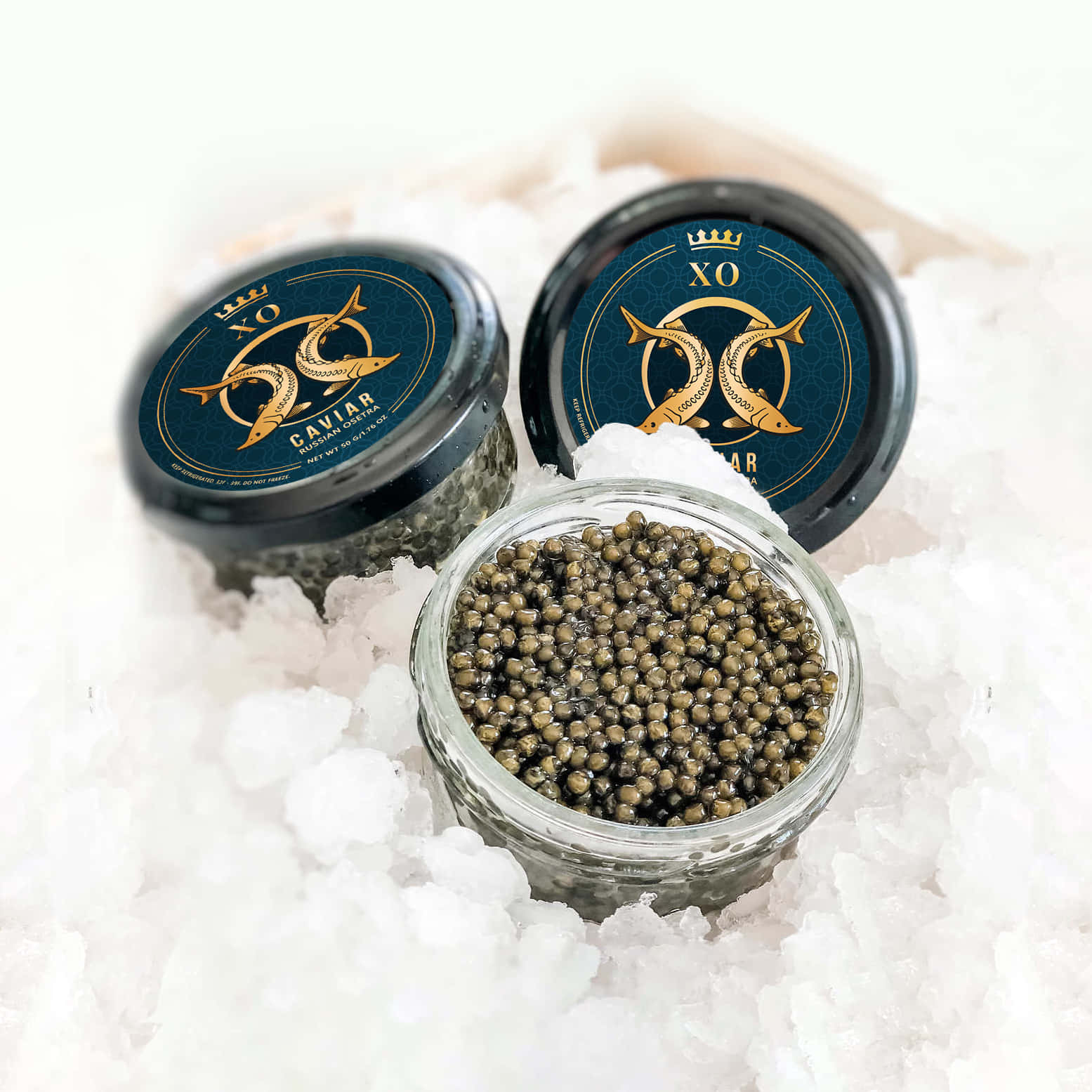 Black Caviar 桌布 壁紙 — 三個帶有金魚標誌的奢華XO魚子醬罐放在碎冰上，其中一個打開，露出閃閃發光的黑色珍珠。
