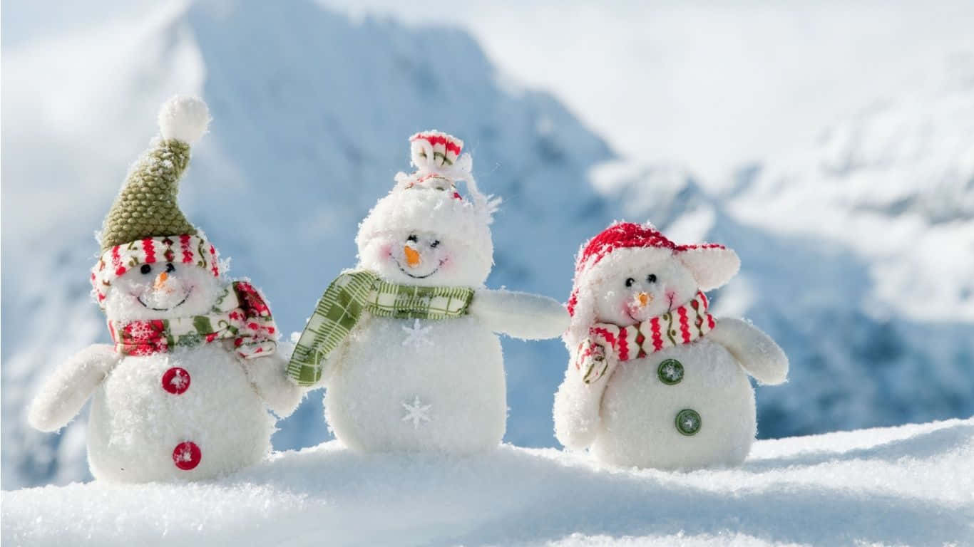 Winter Holiday 桌布 壁紙 — 三個戴著節日帽子和圍巾的快樂雪人公仔在明亮的陽光下手牽手站在白雪皚皚的山坡上。