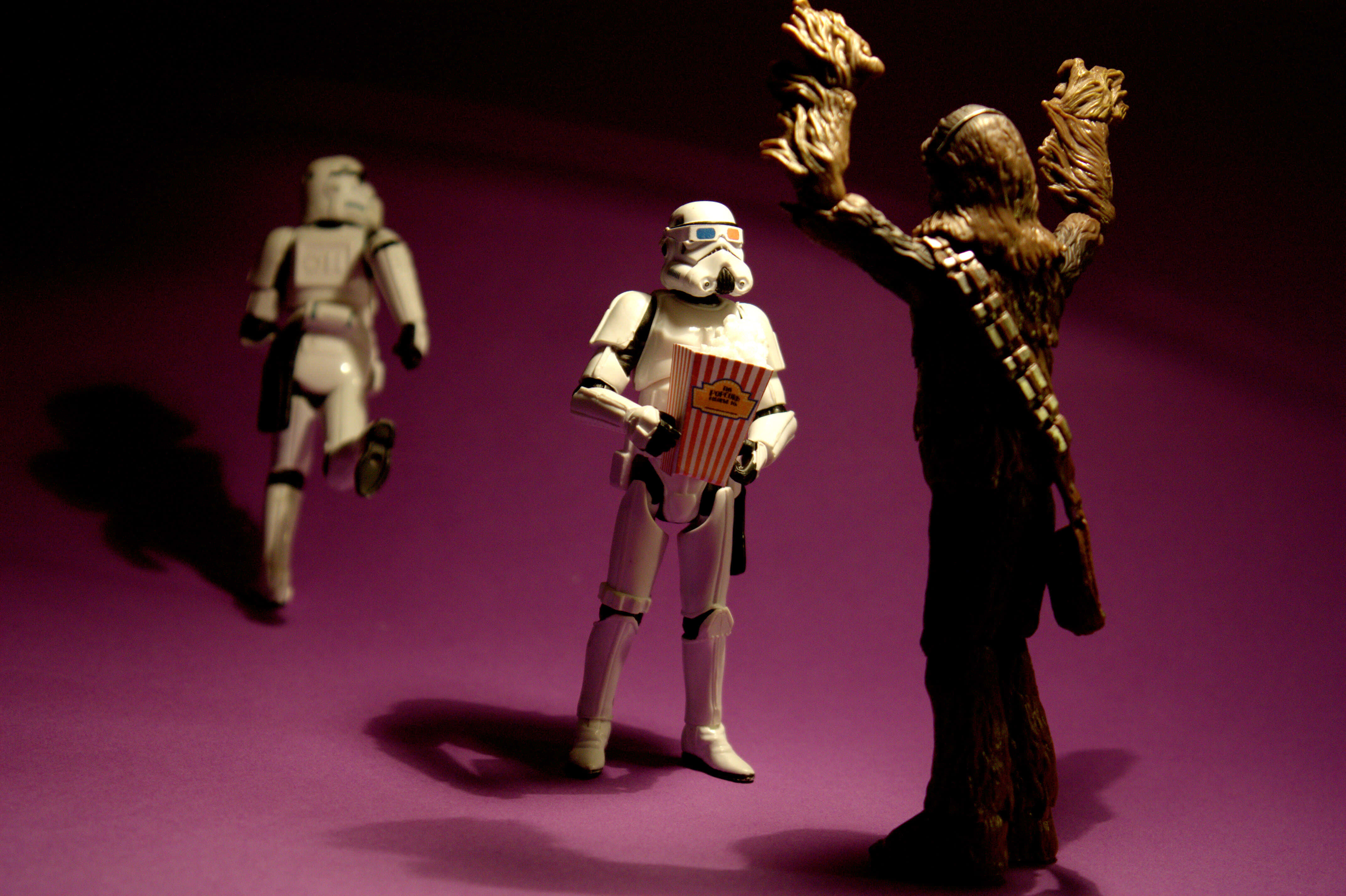 Wookiee 桌布 壁紙 — 三個星戰人偶：一個暴風兵拿著爆谷，和丘巴卡舉起手臂，站在紫色表面上，在戲劇性的燈光下。