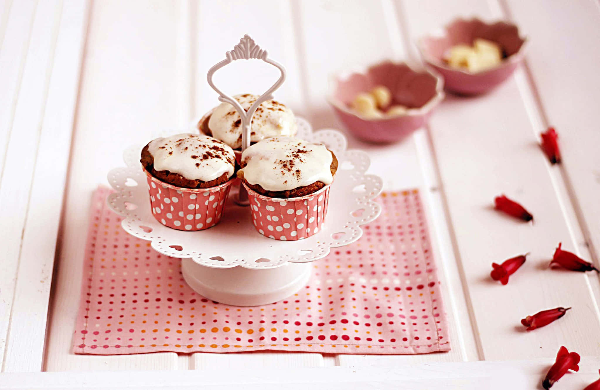 Cute Cupcake 桌布 壁紙 — 三個有糖霜的杯子蛋糕放在粉紅色圓點紙托上，置於白色蕾絲架，架下是圖案餐巾，散落著紅色花瓣。