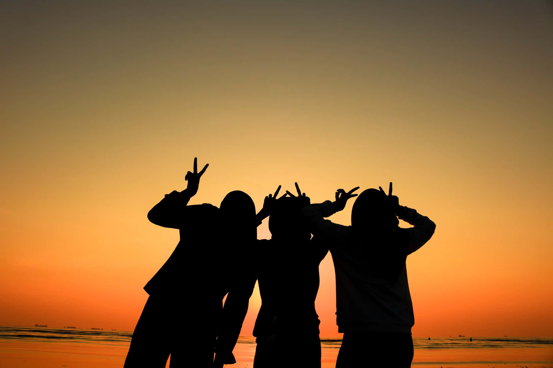 squad 桌布 壁紙 — 三個朋友在海灘上以鮮豔的橙色日落為背景，擺出和平手勢的剪影。