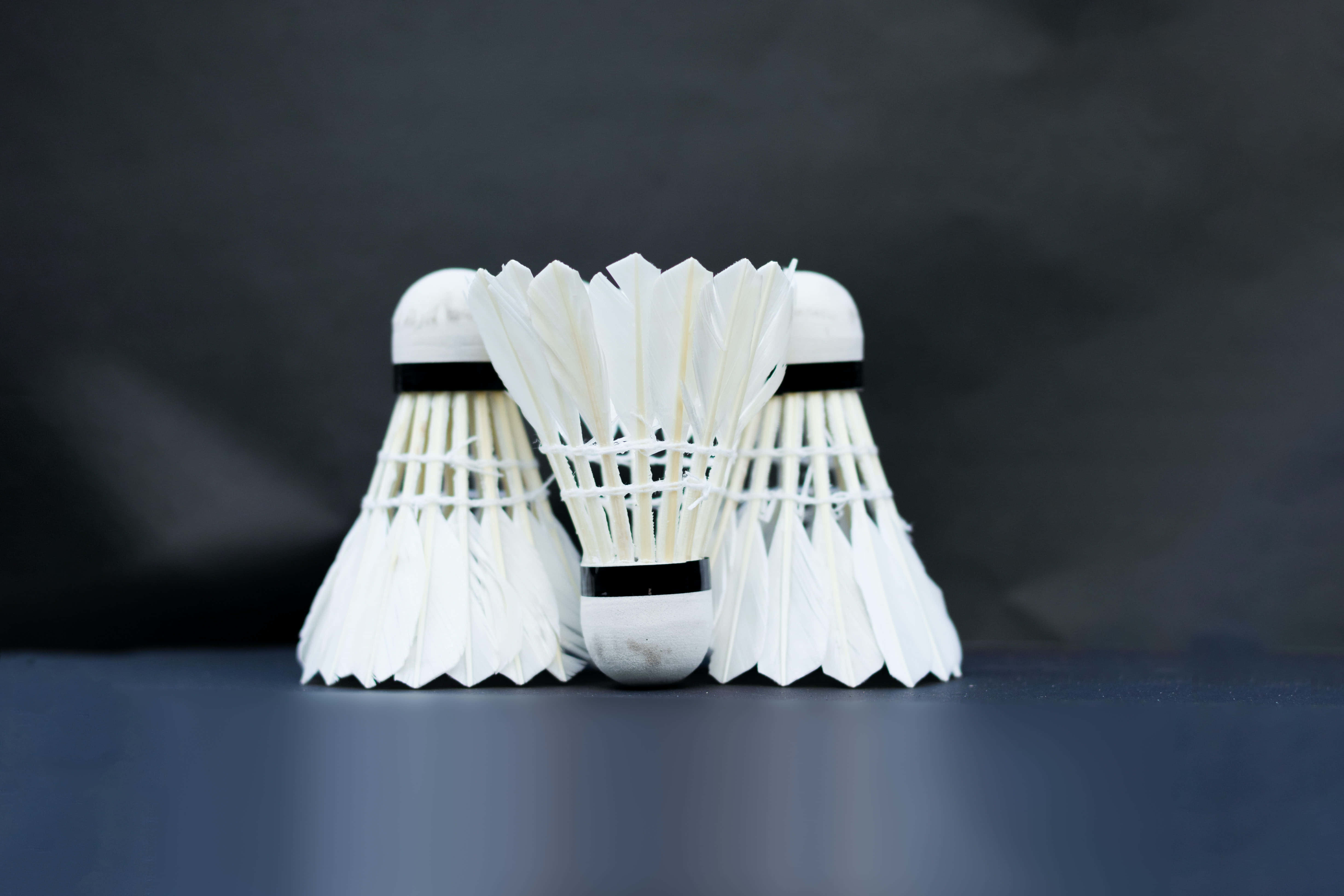Badminton 桌布 壁紙 — 三個白色羽毛球在深色表面上以三角形排列，背景為煙灰色。