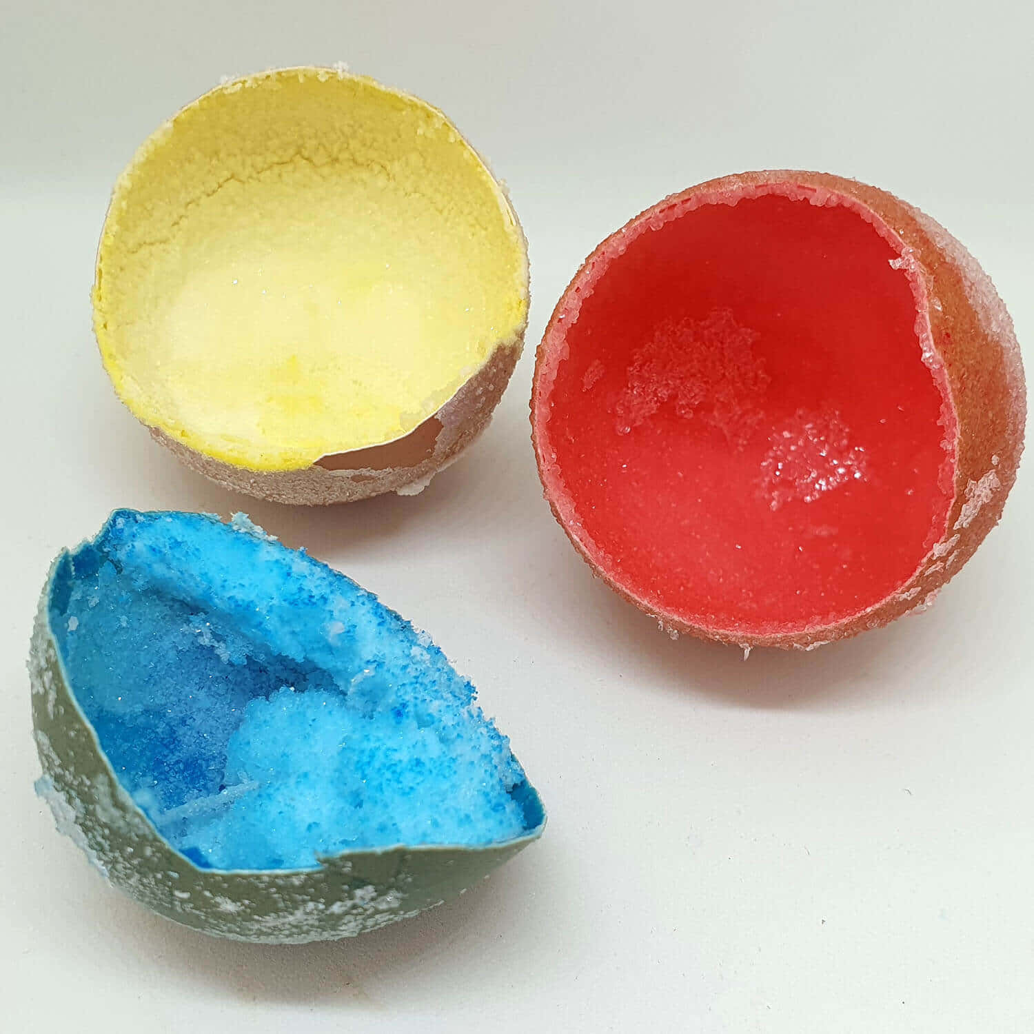 Eggshell 桌布 壁紙 — 三個破裂的浴球在潔白背景上展現出鮮豔的黃色、紅色和藍色內部。
