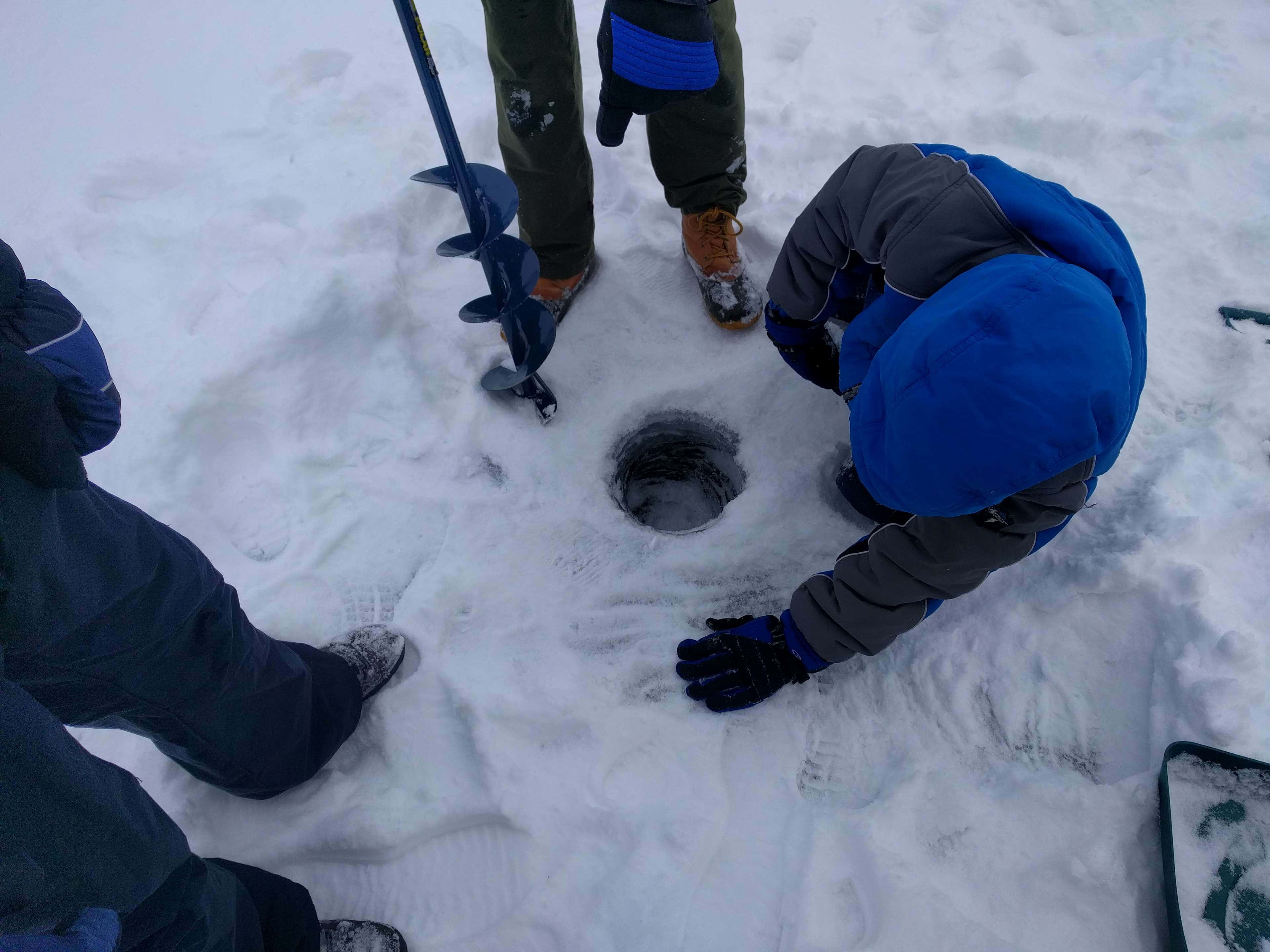 Ice Fishing 桌布 壁紙 — 三個穿著冬季裝備的人在厚雪中鑽孔進行冰釣。