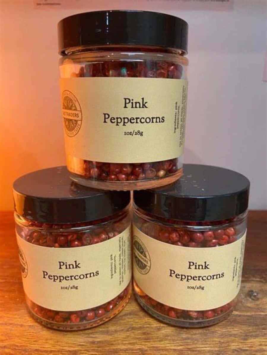 Pink Peppercorn 桌布 壁紙 — 三個粉紅胡椒粒罐頭堆疊在木質表面上，帶有溫暖的環境燈光。