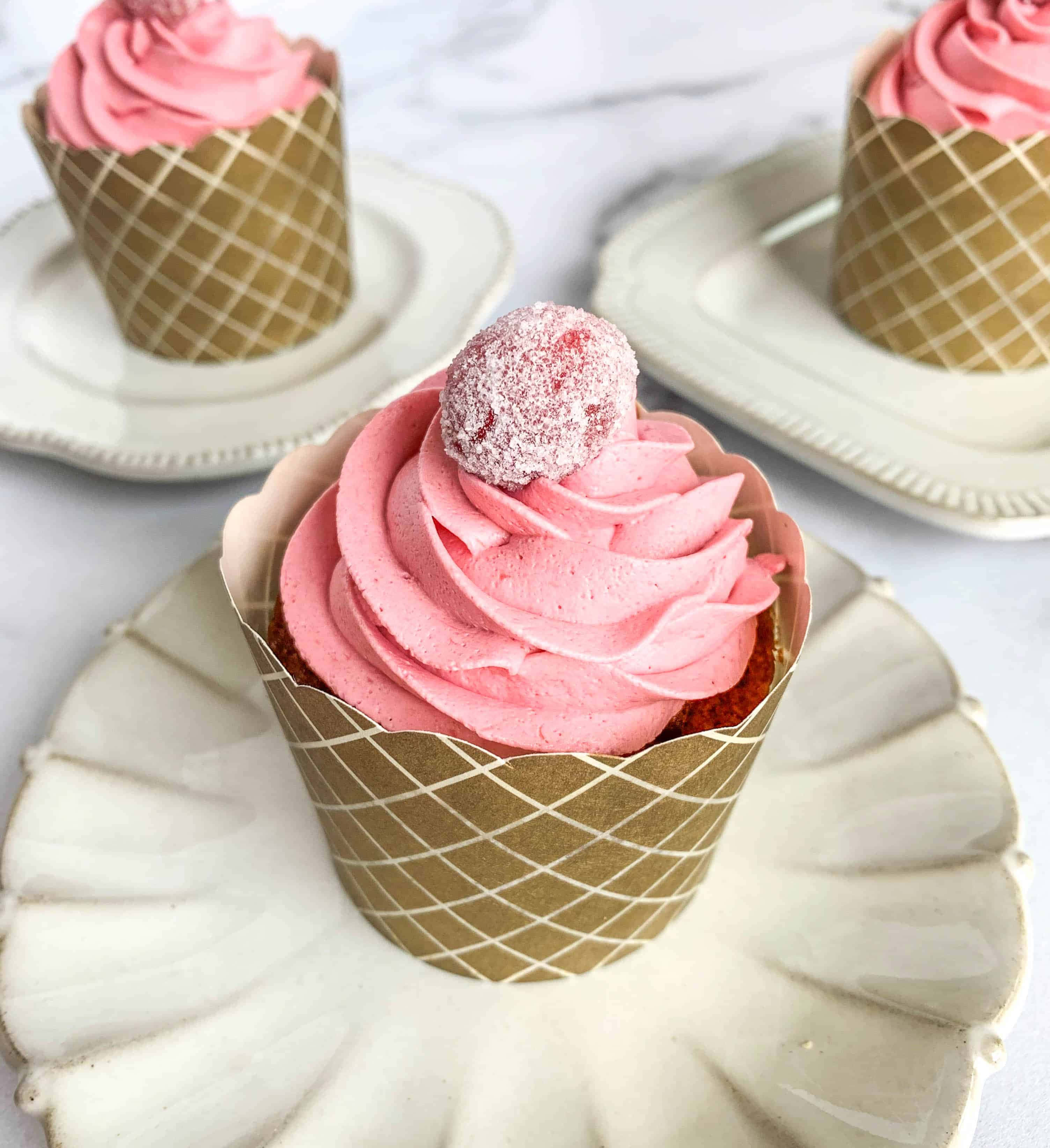 Pink Cupcakes 桌布 壁紙 — 三個粉紅色糖霜杯子蛋糕放在金色格子襯紙中，優雅地置於白色扇貝邊碟子上，背景為大理石。