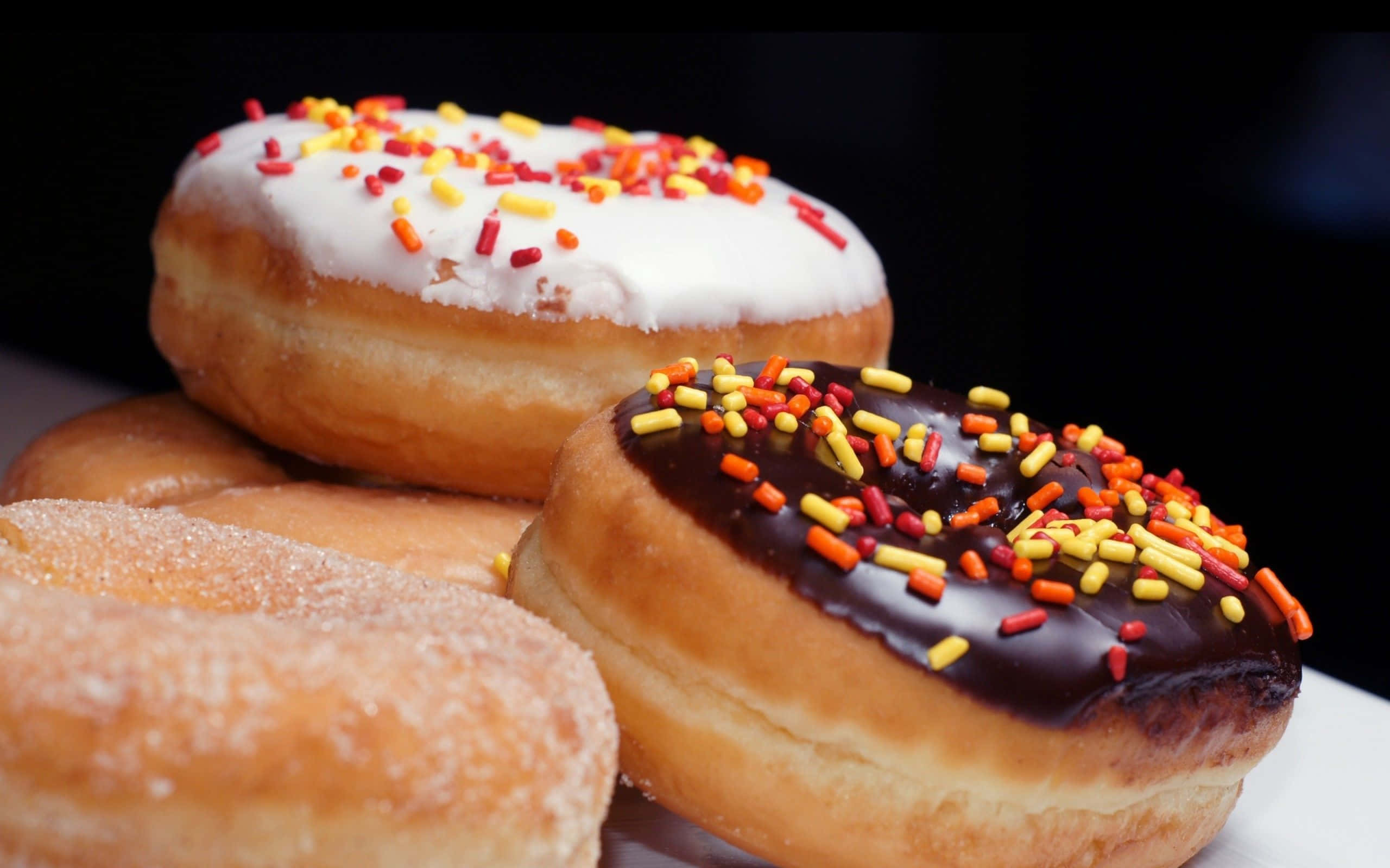 donuts 桌布 壁紙 — 三個糖霜彩針冬甩疊放在白色碟上，背景深色。