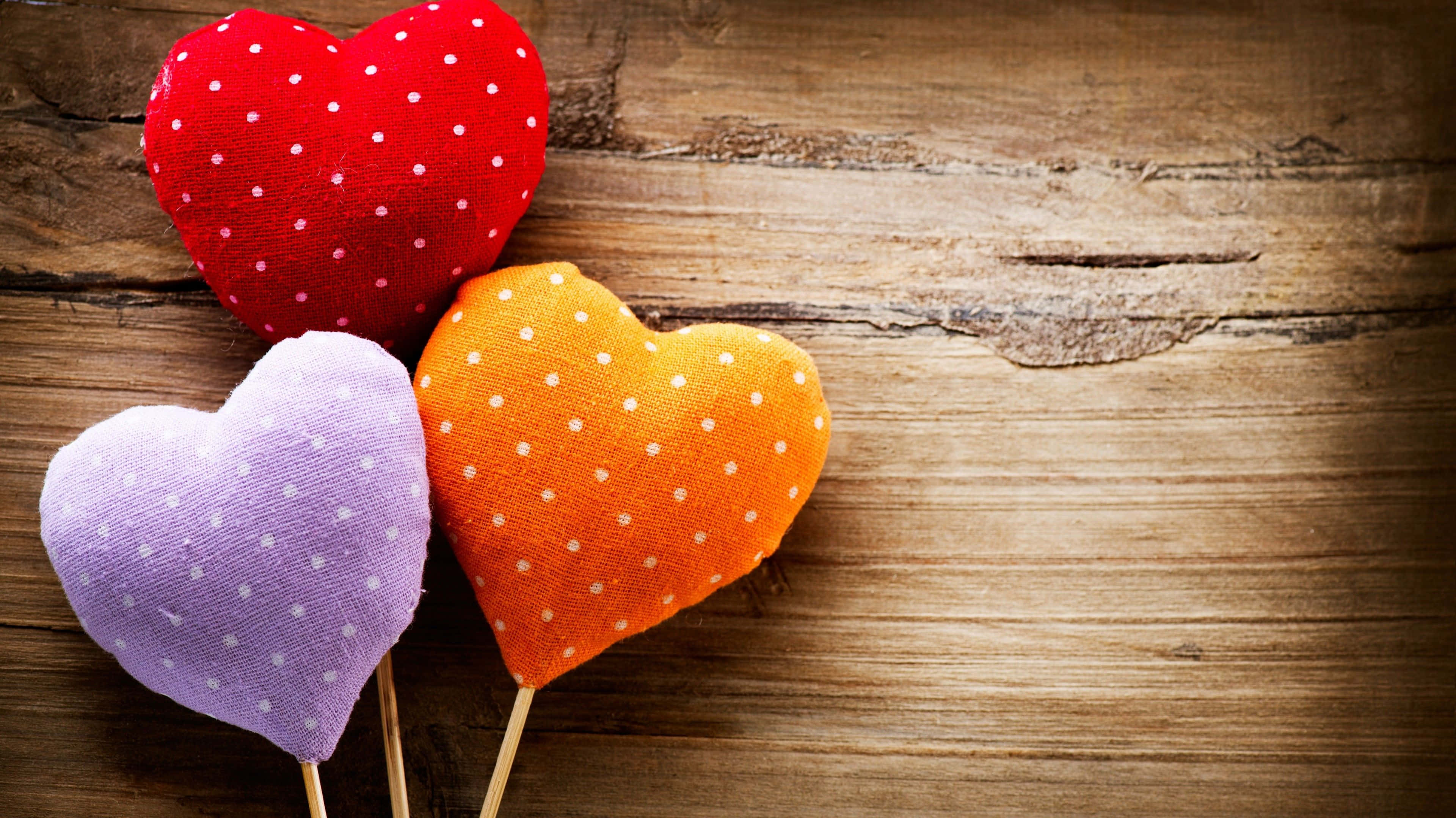 4K Love 桌布 壁紙 — 三個紅色、紫色和橙色帶白色圓點的布料心形，放在木棍上，以質樸的木質背景襯托。
