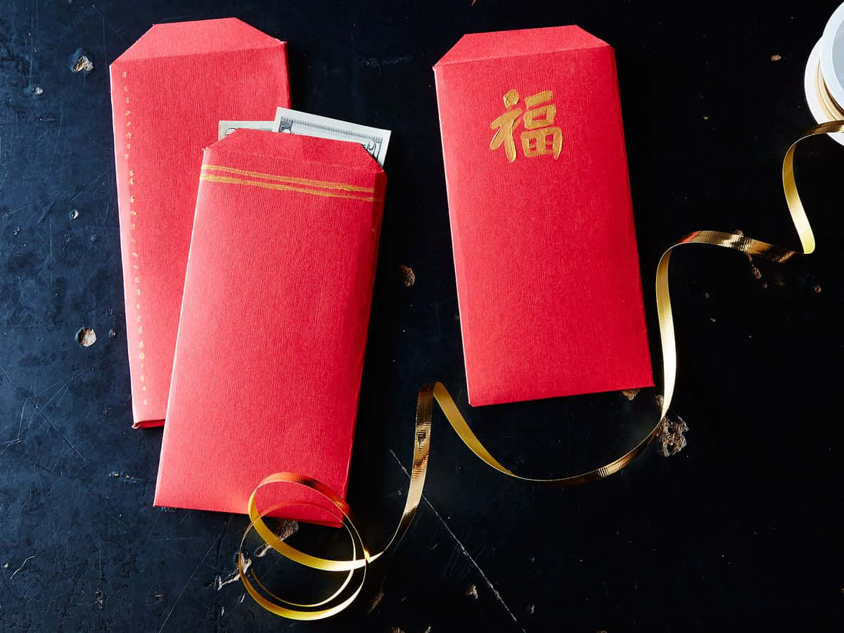 Red Envelope 桌布 壁紙 — 三個紅色中式利是封，金色邊框，其中一個印有「福」字，放在深色紋理表面上，旁邊有一條金色絲帶。