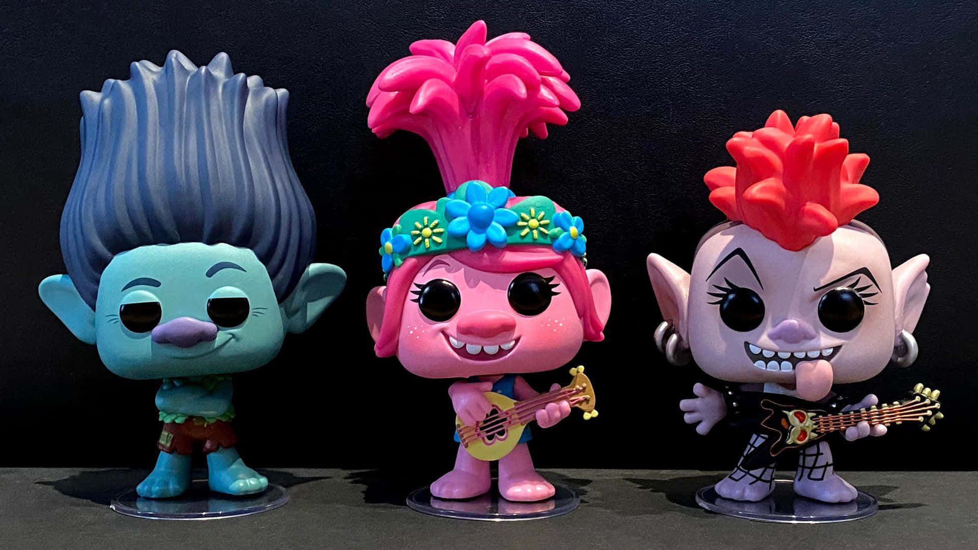 魔髮精靈 桌布 壁紙 — 三個色彩繽紛的 Trolls 角色 Funko Pop! 人偶在深色背景前拿著結他擺姿勢。