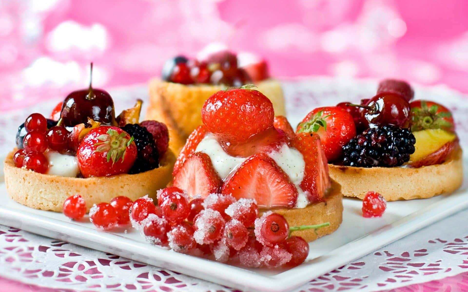 Pastry 桌布 壁紙 — 三個色彩繽紛的水果撻，上面鋪滿士多啤梨、車厘子和黑莓，放在白色碟子上，襯托柔和的粉紅色背景。