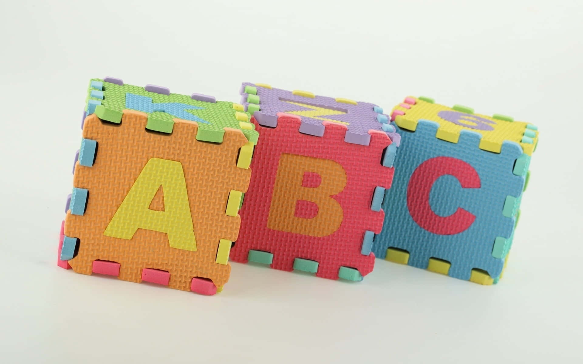 Educational Games 桌布 壁紙 — 三個色彩繽紛的泡沫字母積木拼出ABC，放在純白表面上。