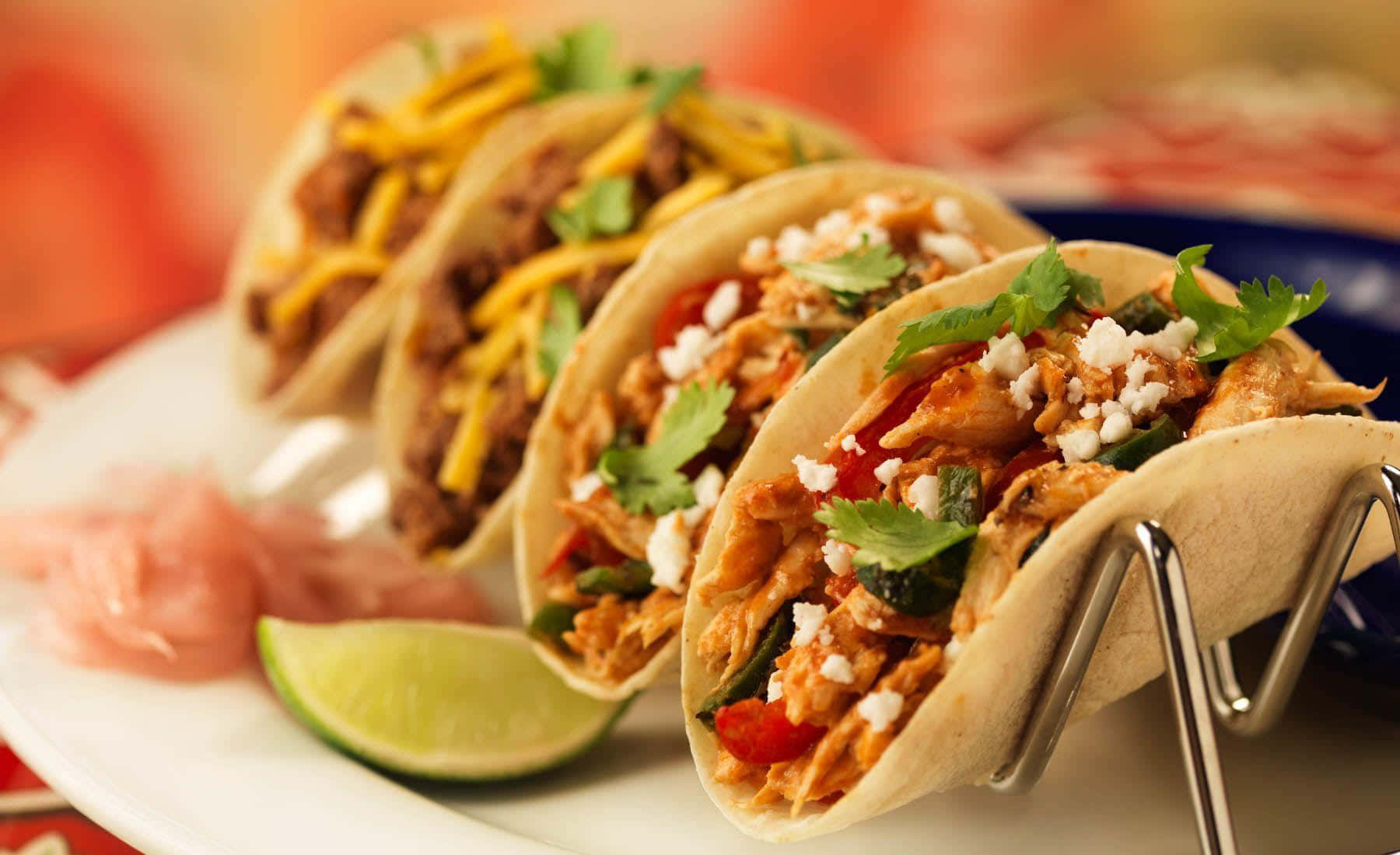 Taco 桌布 壁紙 — 三個色彩繽紛的雞肉玉米餅，飾以芫荽和芝士，放在金屬架上，置於配有青檸和醃洋蔥的碟上。