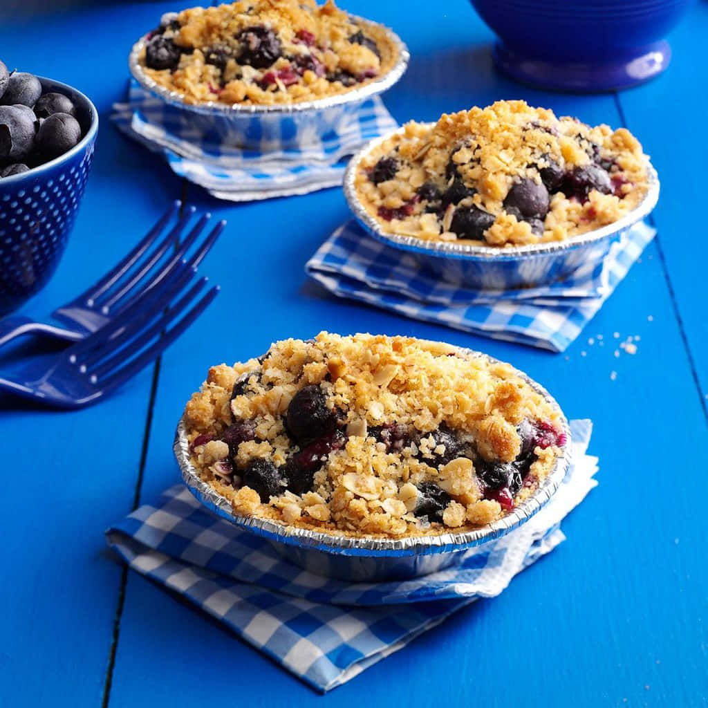 Blueberries Tart 桌布 壁紙 — 三個藍莓金寶批放在錫紙盤上，置於格仔餐巾上，再放在鮮藍色木桌上。