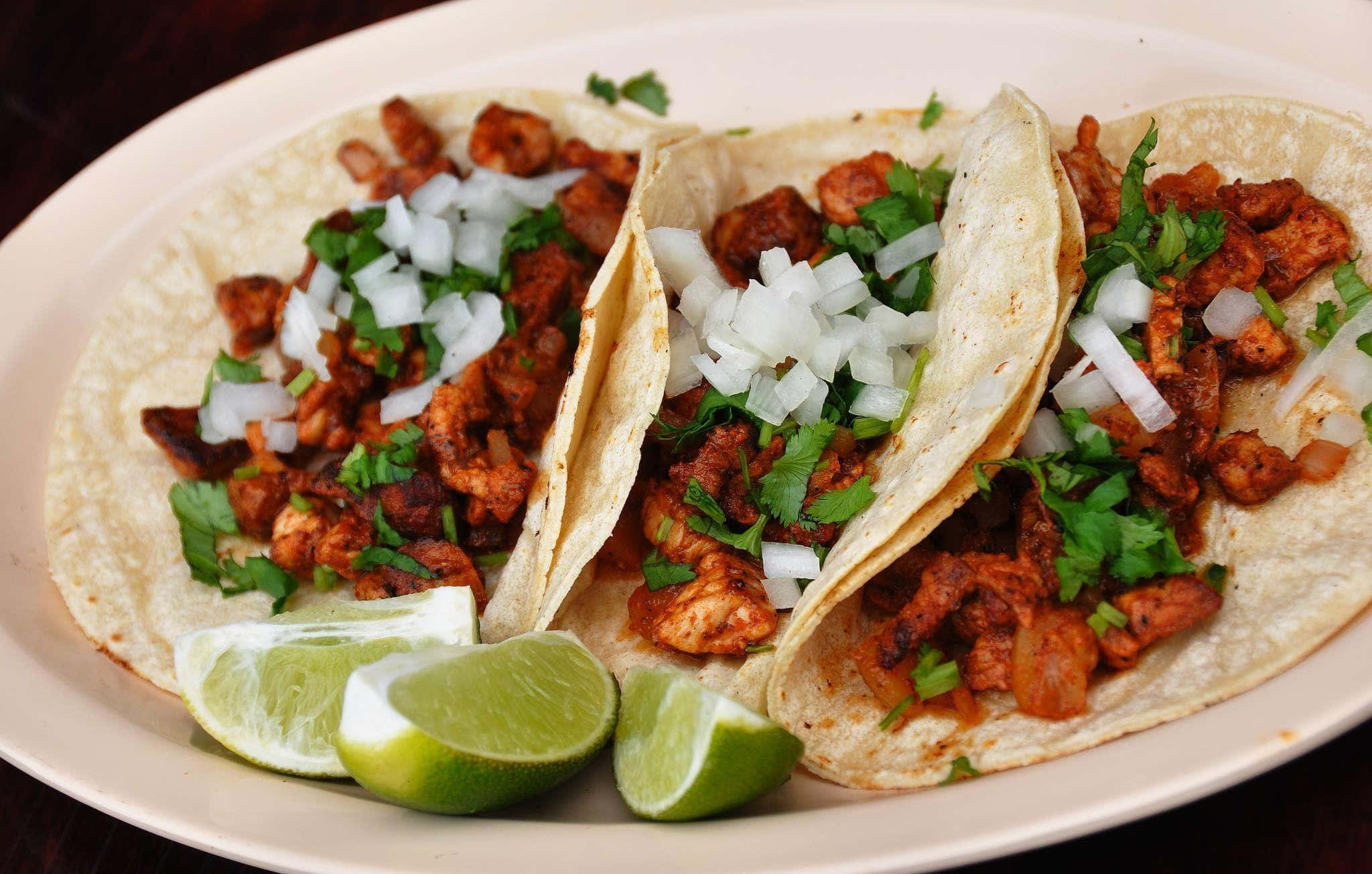 Taco 桌布 壁紙 — 三個軟玉米餅，內餡為調味肉、香菜和洋蔥，搭配青檸角，盛於白盤中。