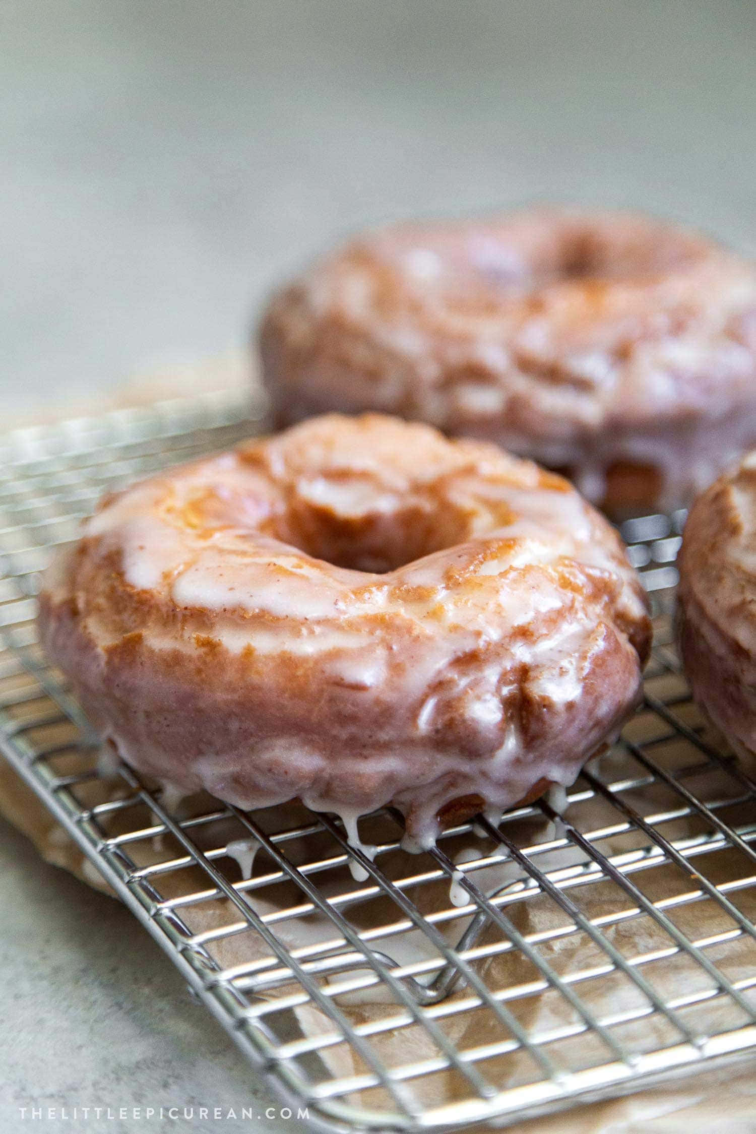 Glazed Donut 桌布 壁紙 — 三個釉面肉桂冬甩放在金屬冷卻架上，閃亮的糖霜沿邊滴落。