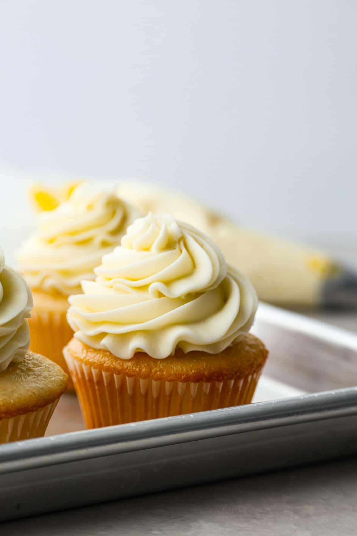 Buttercream 桌布 壁紙 — 三個金色紙杯蛋糕，上面有奶油香草糖霜漩渦，放在金屬烤盤上。