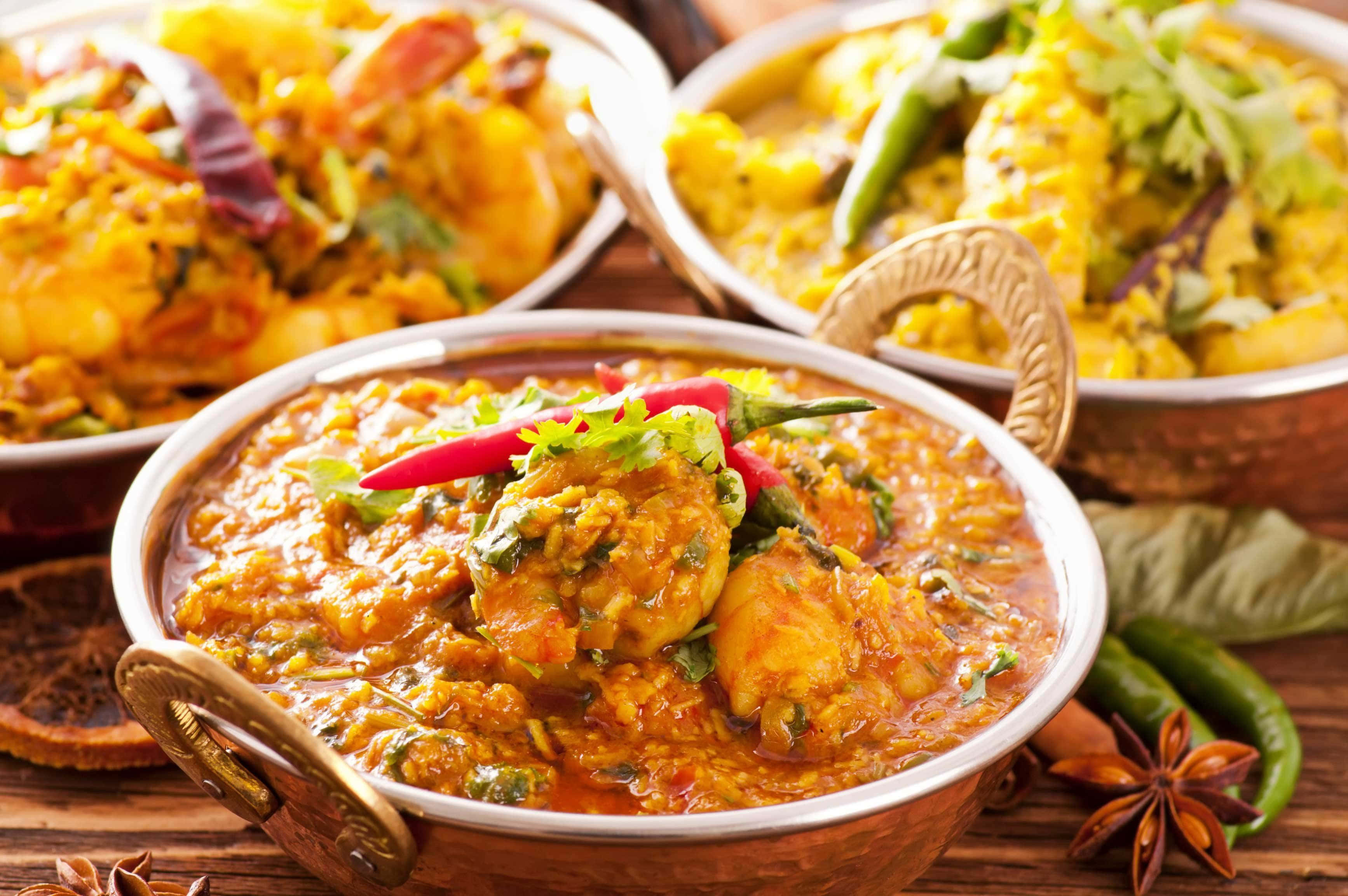 Indian Food 桌布 壁紙 — 三個銅碗盛滿香料豐富的印度咖喱，上面裝飾著新鮮的芫荽和紅辣椒，放在質樸的木桌上。