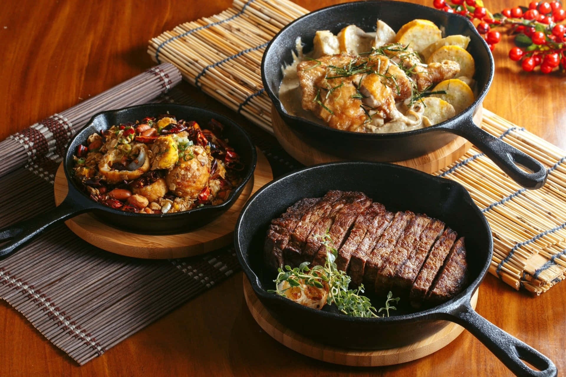Lunch 桌布 壁紙 — 三個鑄鐵煎鍋展示多汁牛排、奶油雞肉和辣味炒菜，放在溫暖的木桌上，配有竹蓆和紅莓。
