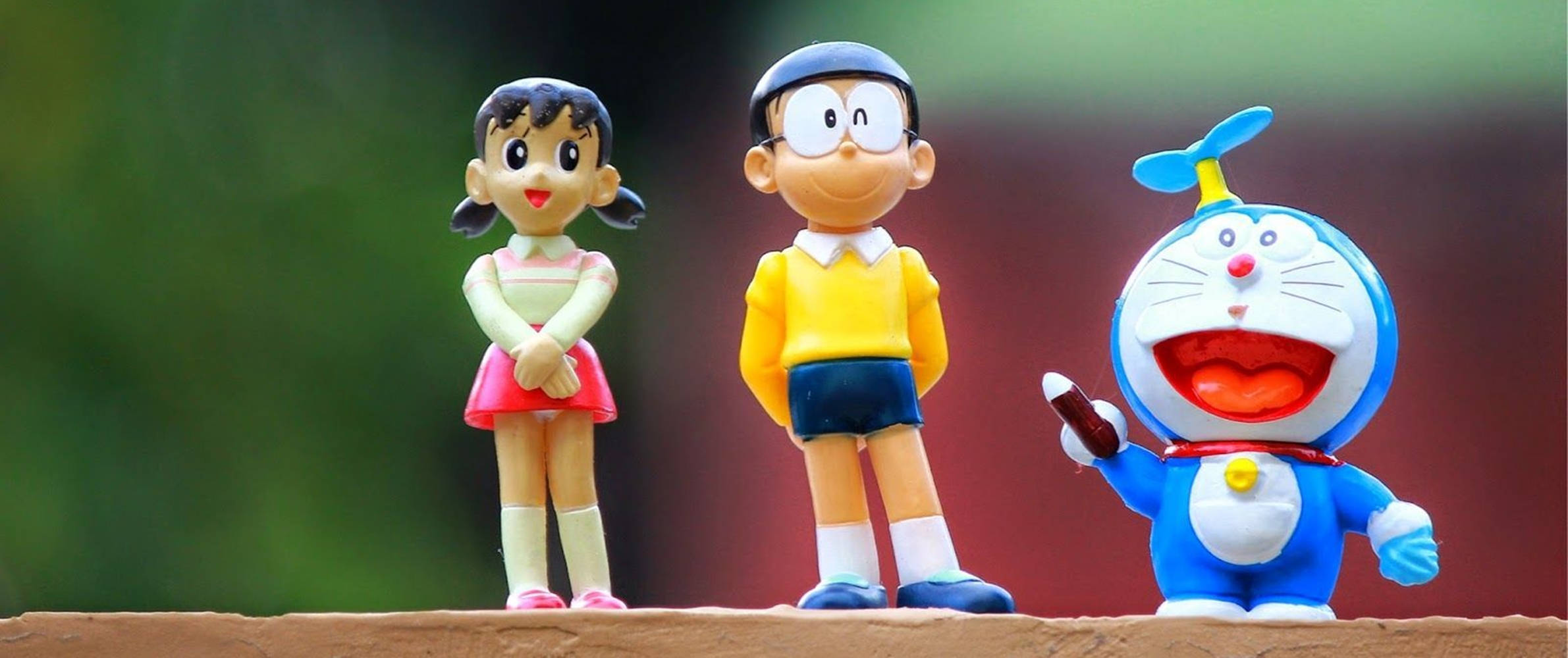 nobita 桌布 壁紙 — 三個開心嘅多啦A夢動畫公仔一齊企喺木質表面上，背景係模糊嘅綠色同紅色。