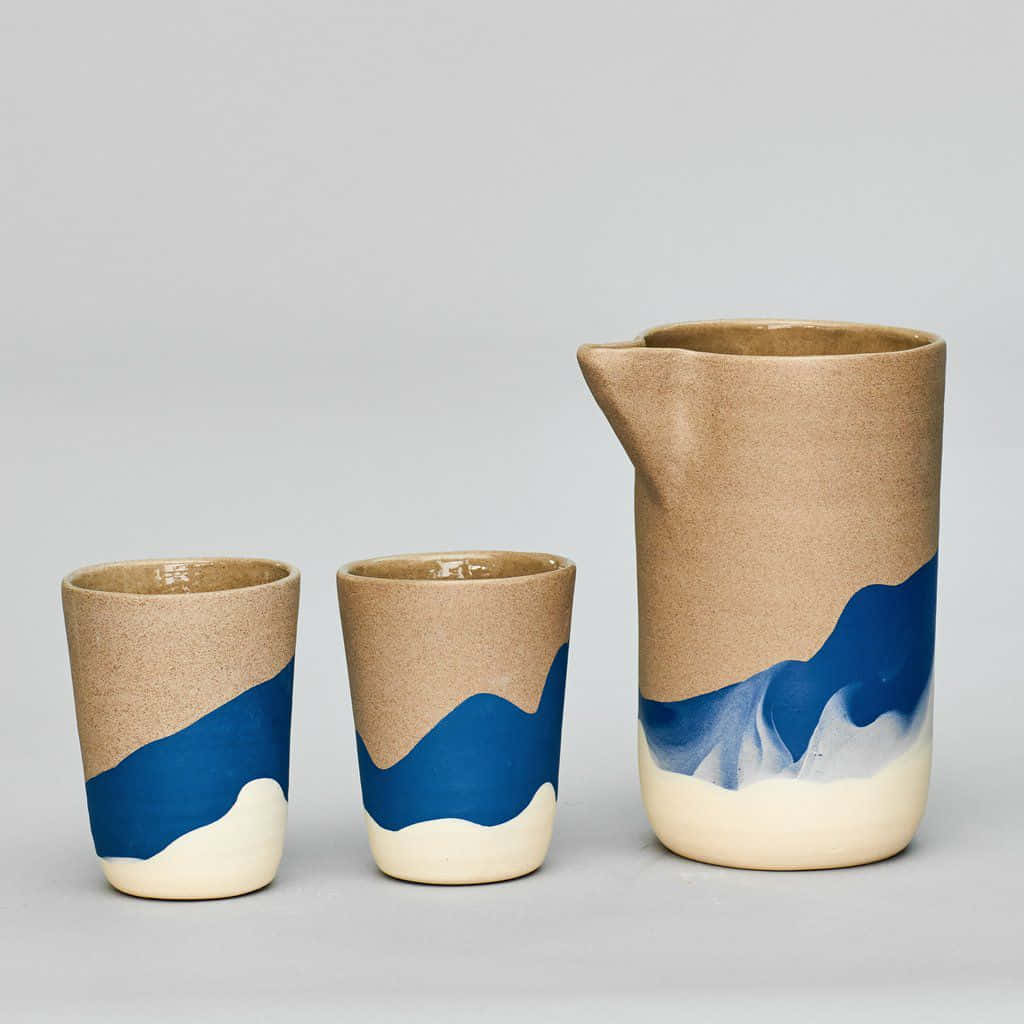 Ceramic 桌布 壁紙 — 三個陶瓷容器，帶有大地色米色和大膽的藍色波浪圖案，置於中性灰色背景上。