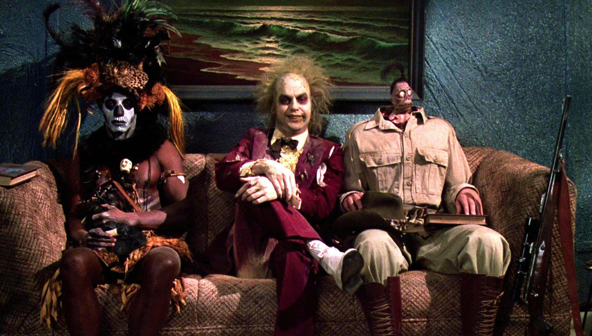 Beetlejuice 桌布 壁紙 — 三個面容塗繪、服飾怪誕的角色坐在昏暗房間的破舊沙發上。