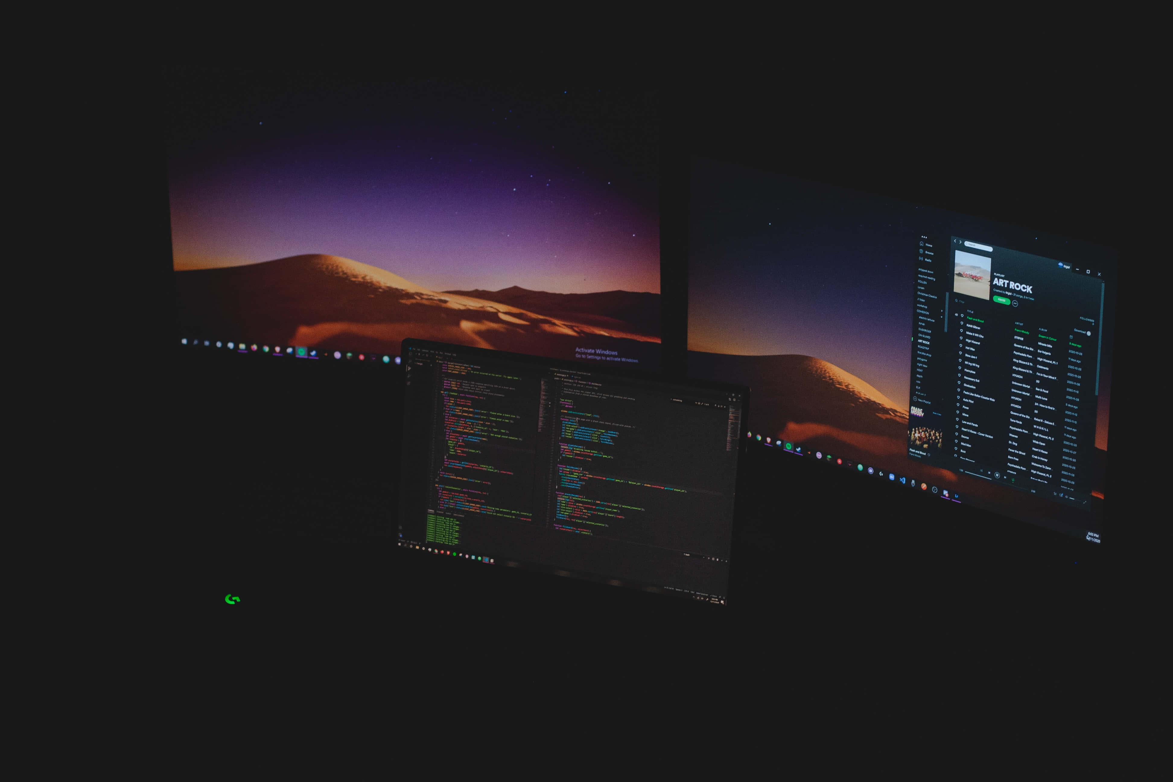 4K Programming 桌布 壁紙 — 三個顯示器在黑暗中發光，顯示代碼編輯器、音樂播放器和山景日落桌布。