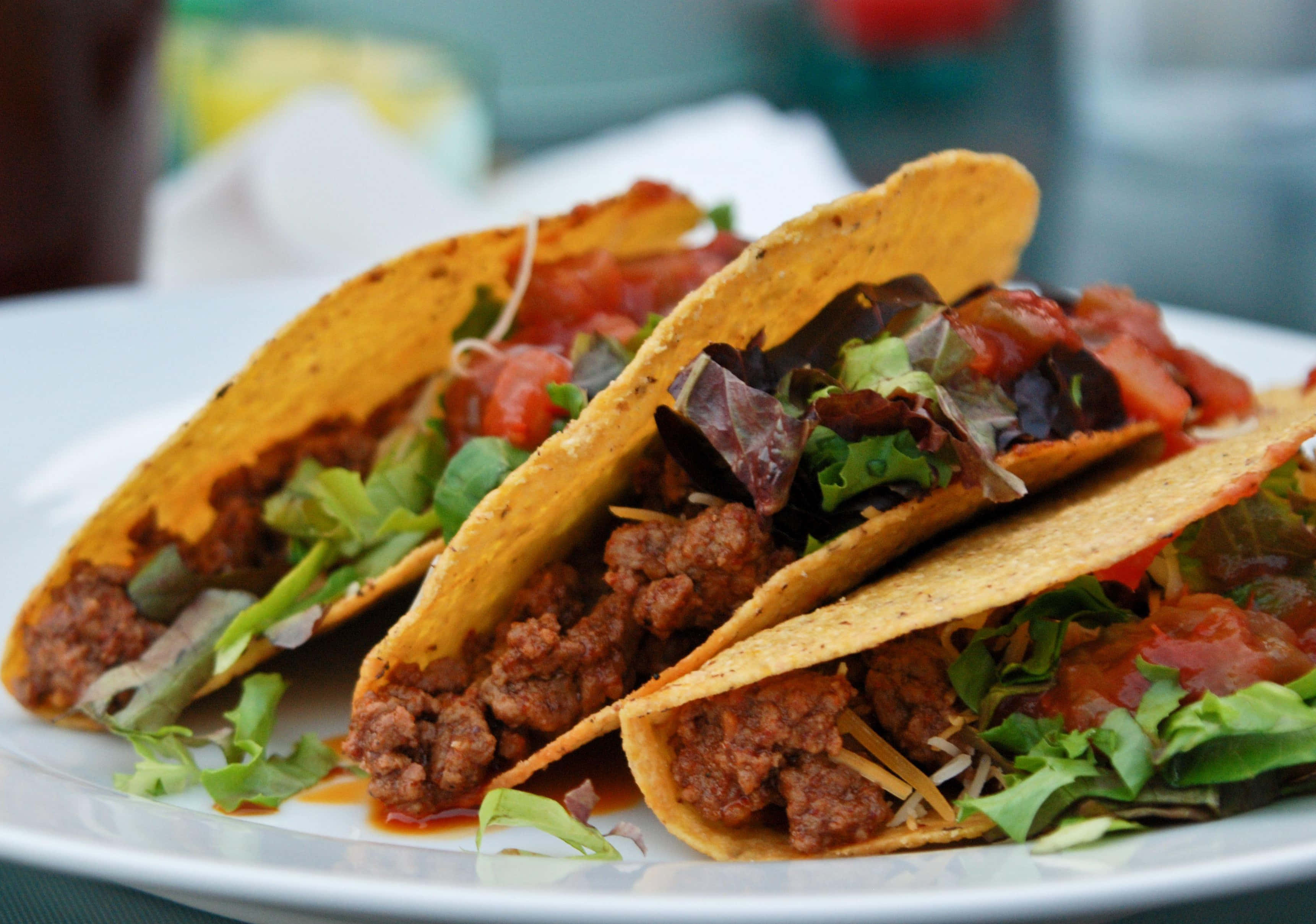 Taco 桌布 壁紙 — 三個香脆的墨西哥卷餅，內餡有調味肉、莎莎醬、生菜和芝士，誘人地放在白色碟子上。