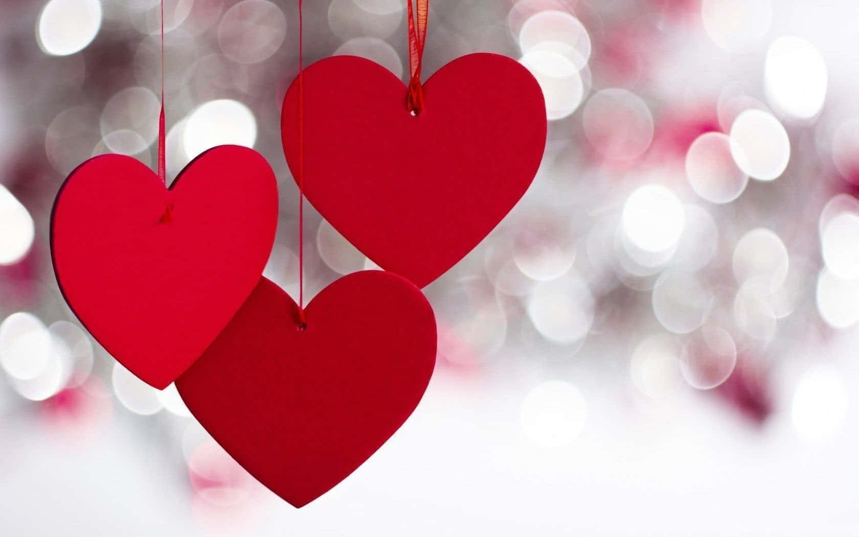 Red Heart 桌布 壁紙 — 三個鮮紅色的紙心心懸掛在閃爍的散景背景上，背景由白色和粉紅色的燈光組成。