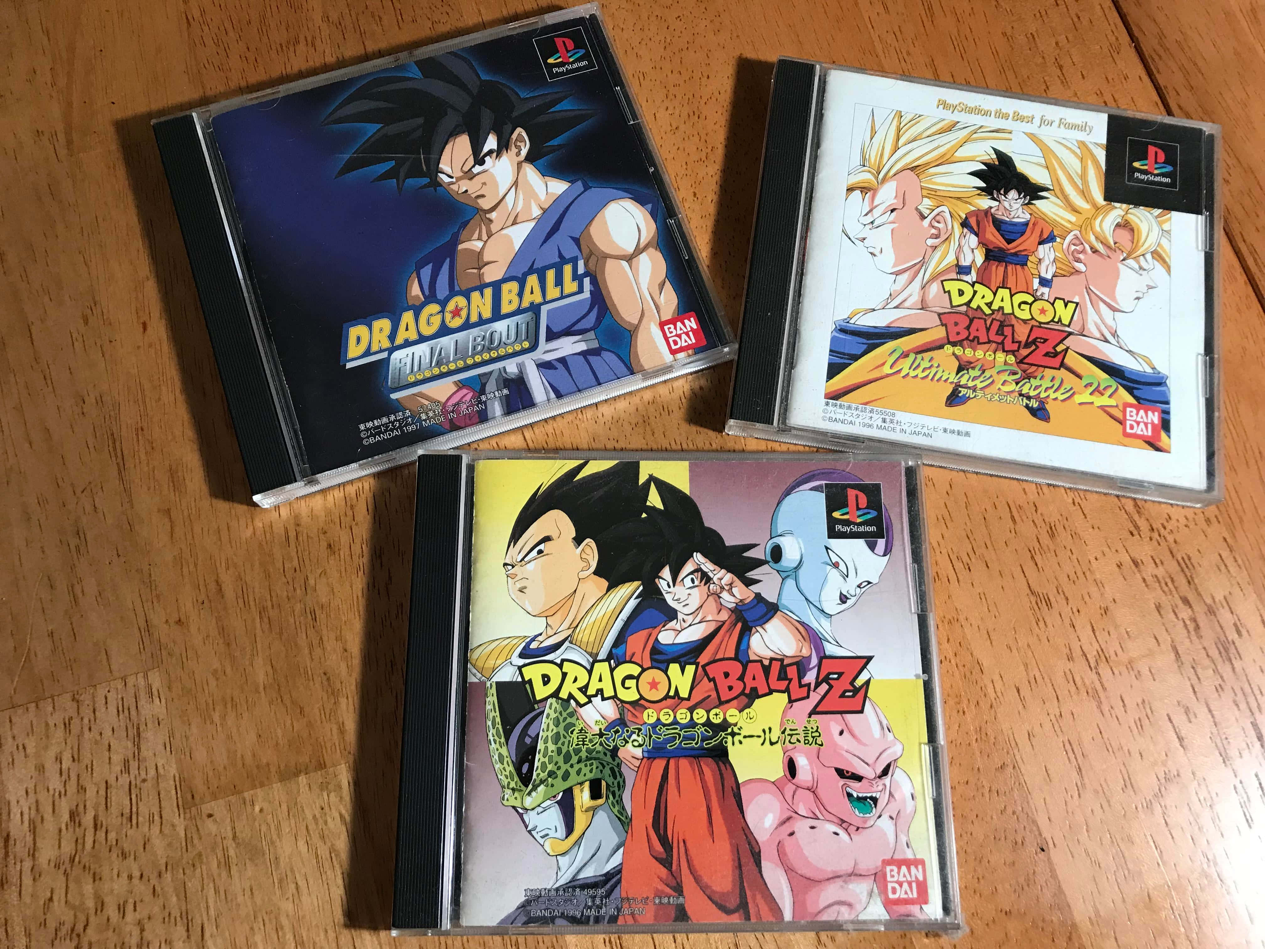 Dbz Video Games 桌布 壁紙 — 三個龍珠Z PlayStation遊戲盒整齊排列在溫暖的木地板上，展示充滿活力的動漫角色封面藝術。