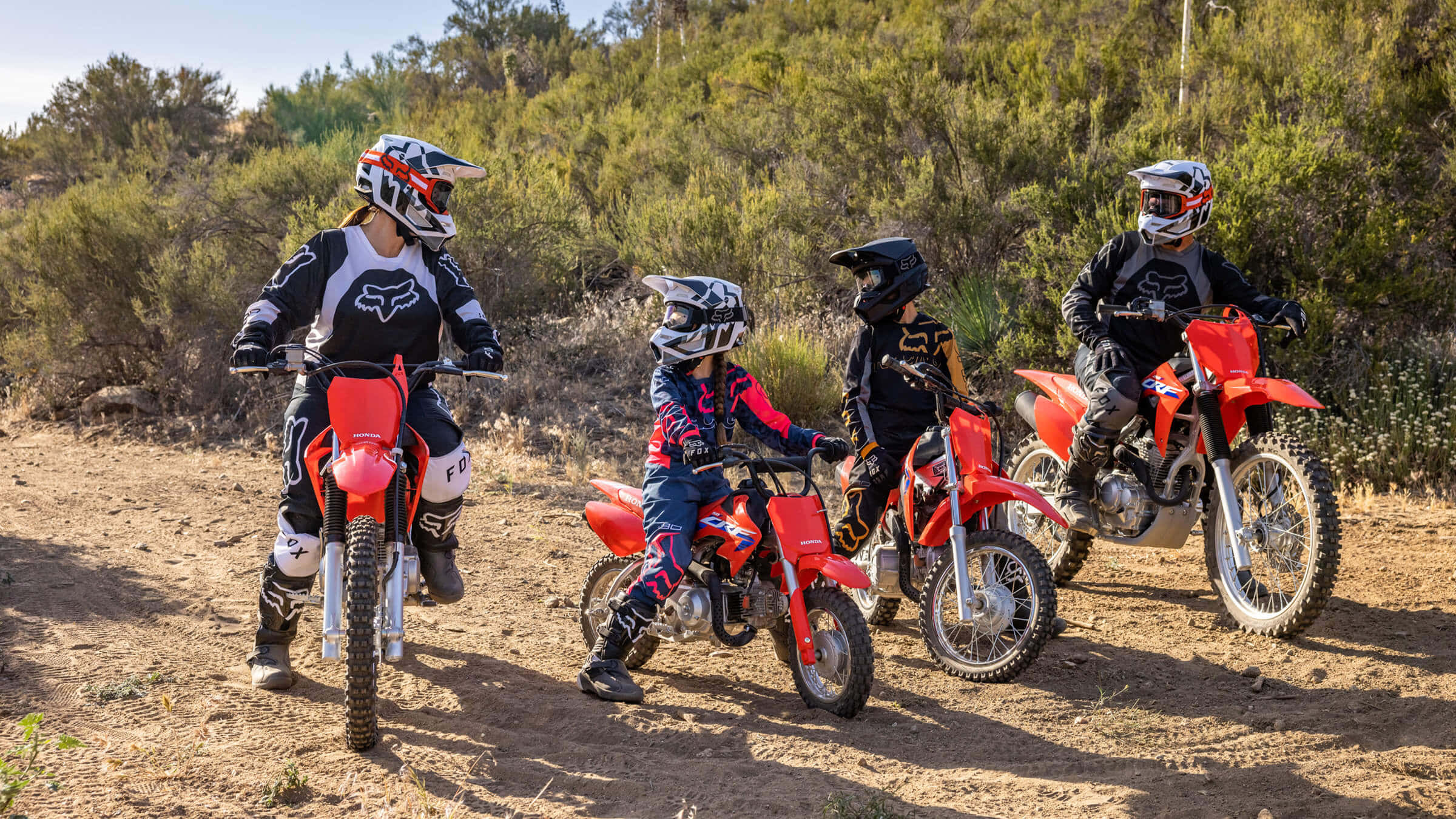 Dirtbike 桌布 壁紙 — 三名全副裝備的騎手在明亮的日光下，在乾燥的灌木叢中停在紅色越野車上。