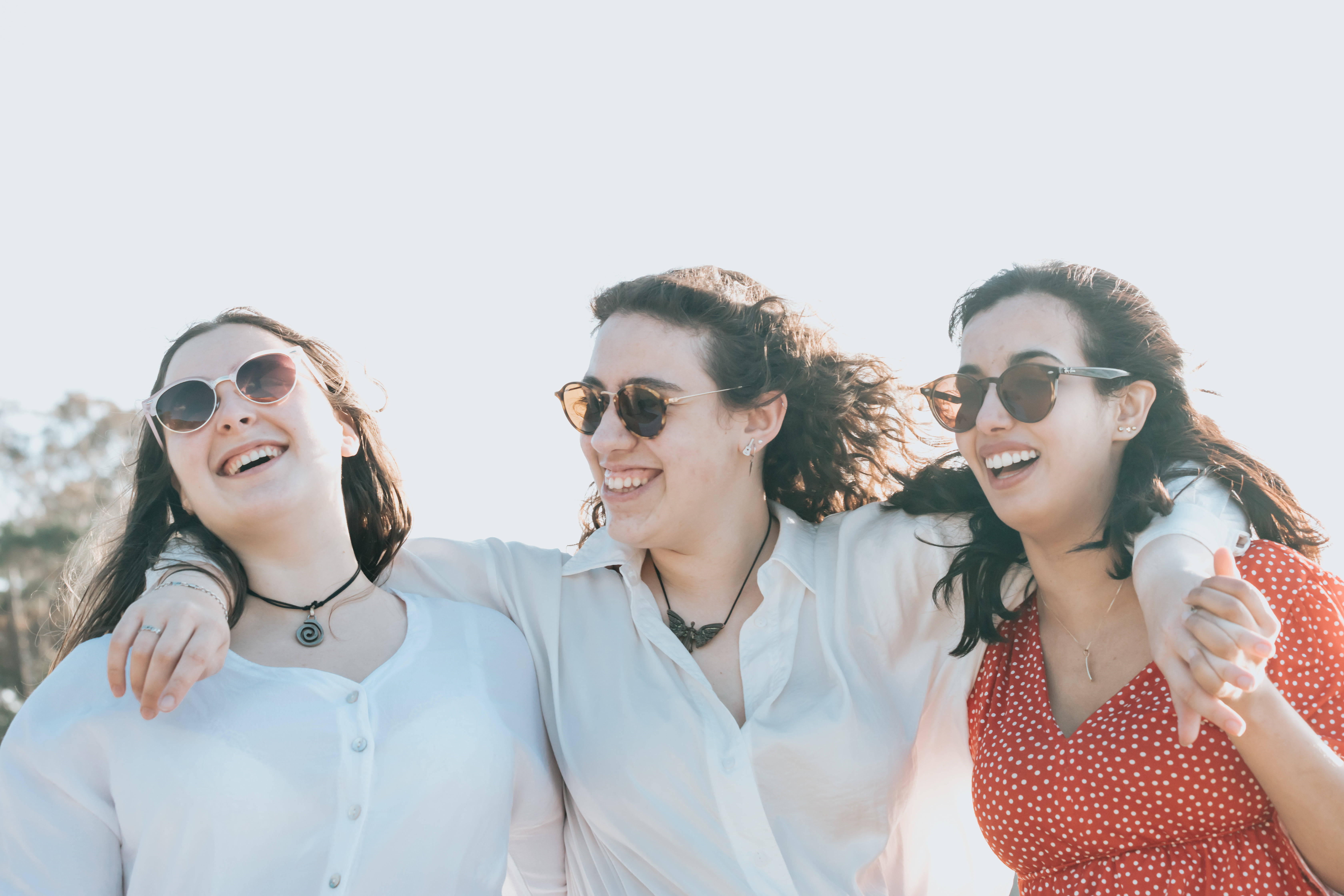 三名快樂女孩的友誼 壁紙 — 三位快樂的朋友在明亮的陽光下戴著太陽眼鏡和休閒夏裝，一起在戶外大笑。