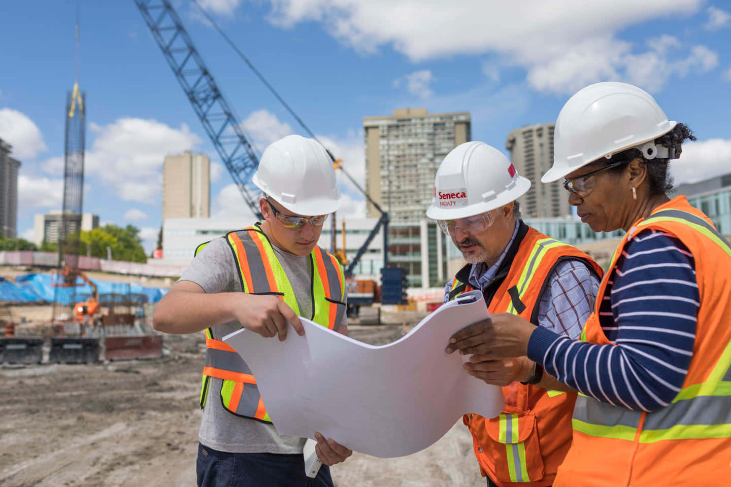 Engineer 桌布 壁紙 — 三名戴著安全帽和反光背心的建築工人在繁忙的城市建築工地，在明亮的藍天下審閱藍圖。