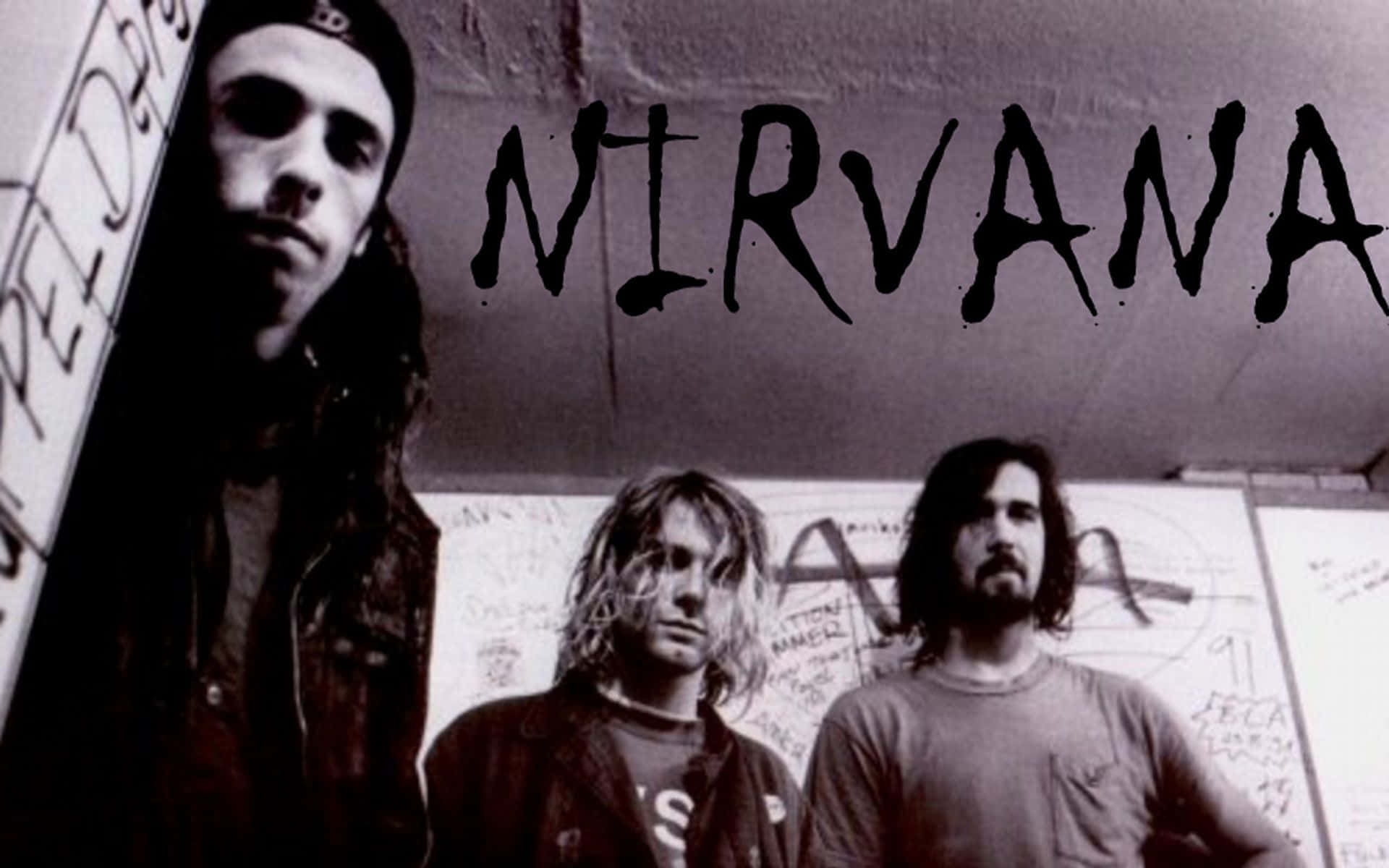 nirvana 桌布 壁紙 — 三名油漬搖滾樂隊成員在佈滿塗鴉的牆前，頭頂有粗體黑色字母 'NIRVANA'，他們專注地凝視著鏡頭。