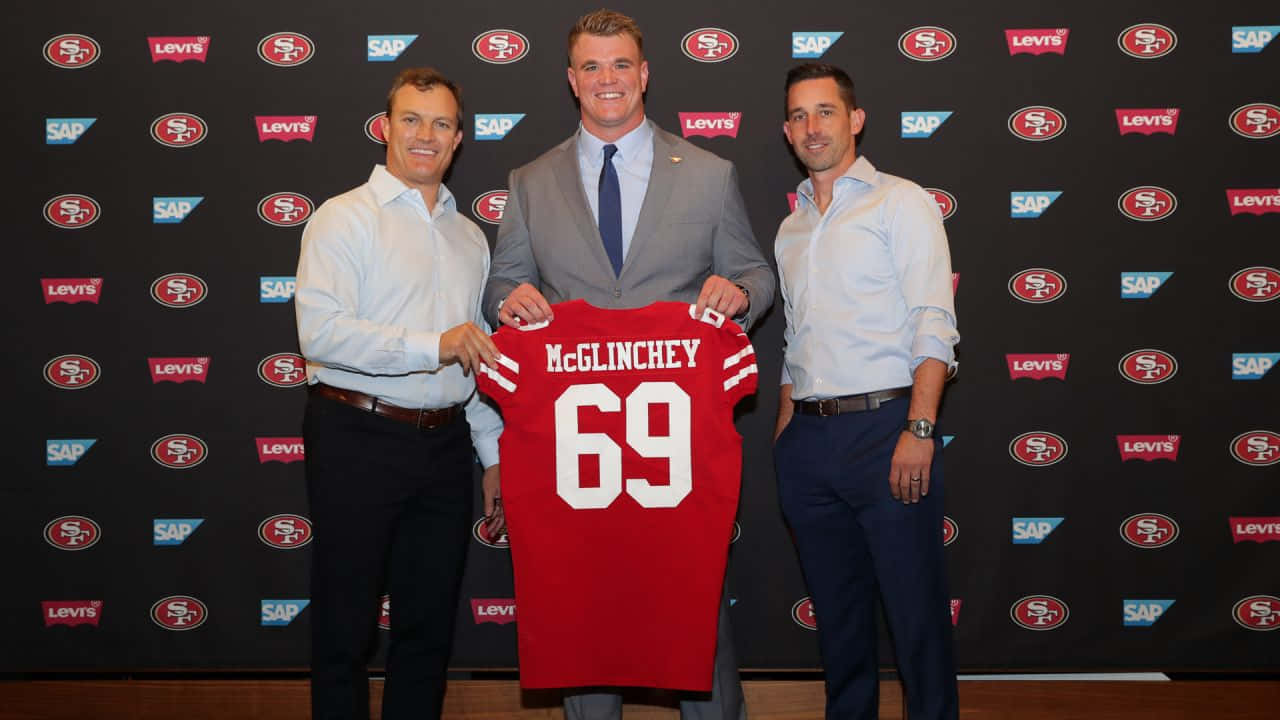 Mike Mcglinchey 桌布 壁紙 — 三名男子在品牌背景前，手持一件印有 McGlinchey 69 的紅色三藩市 49 人隊球衣擺姿勢。