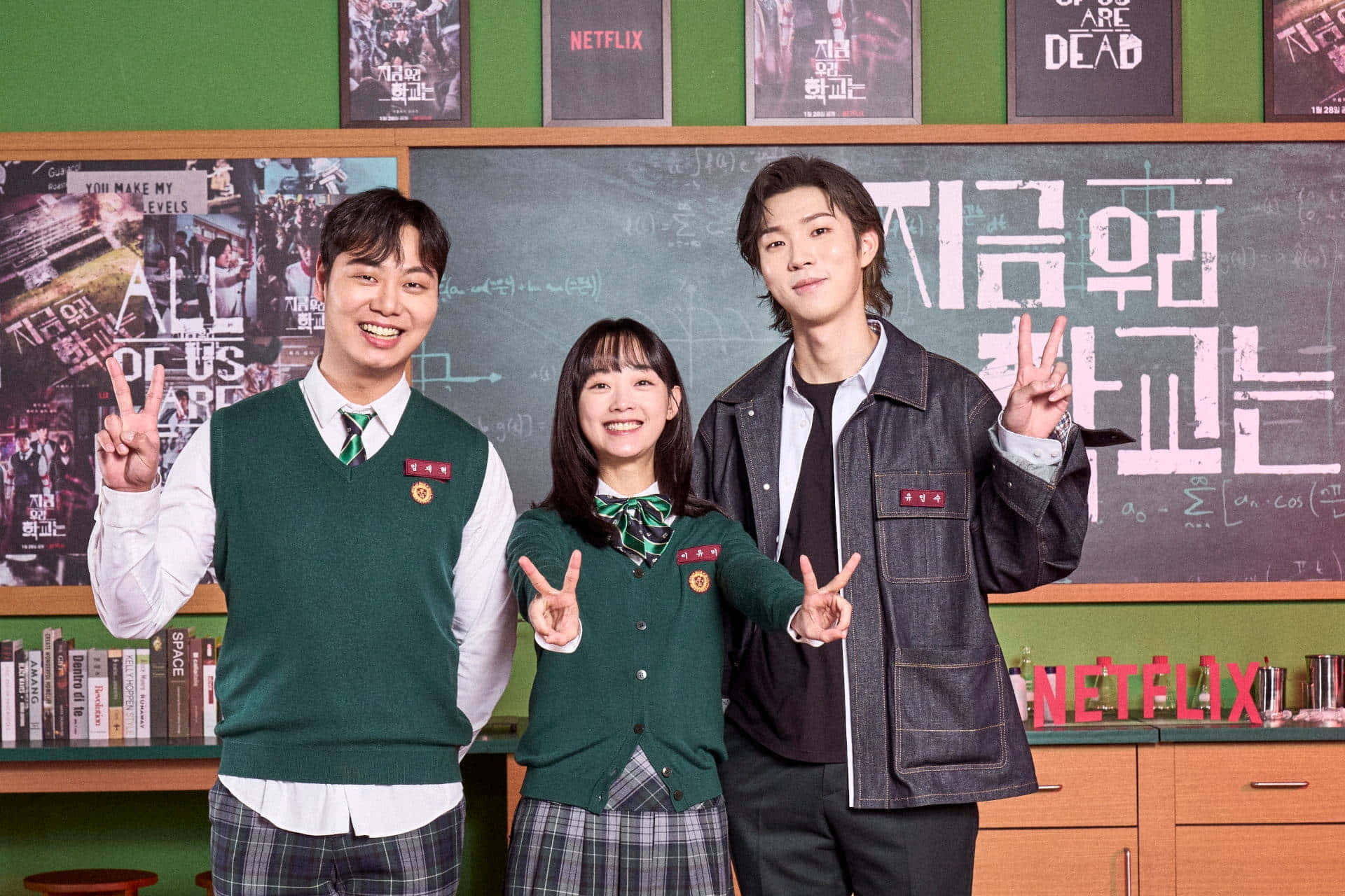 我哋都係死人 桌布 壁紙 — 三名穿著校服的學生在裝飾有Netflix海報和黑板的教室中微笑比出和平手勢。