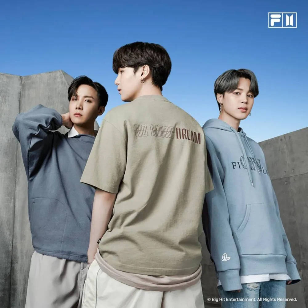 FILA J-Hope、Jimin、Suga 壁紙 — 三名身穿休閒街頭服的年輕男子在晴朗藍天下以混凝土牆為背景擺姿勢。