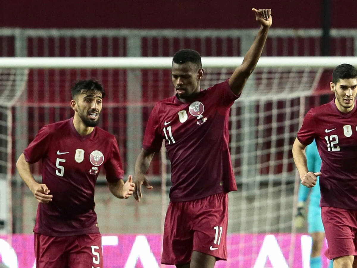 Qatar 桌布 壁紙 — 三名身穿栗紅色球衣的足球員在燈光明亮的球場上高舉雙臂，神情激昂地慶祝入球。