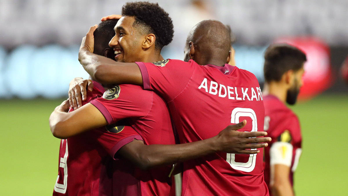 Qatar 桌布 壁紙 — 三名身穿紅色球衣的足球運動員在球場燈光下的綠色草地上歡樂地擁抱。
