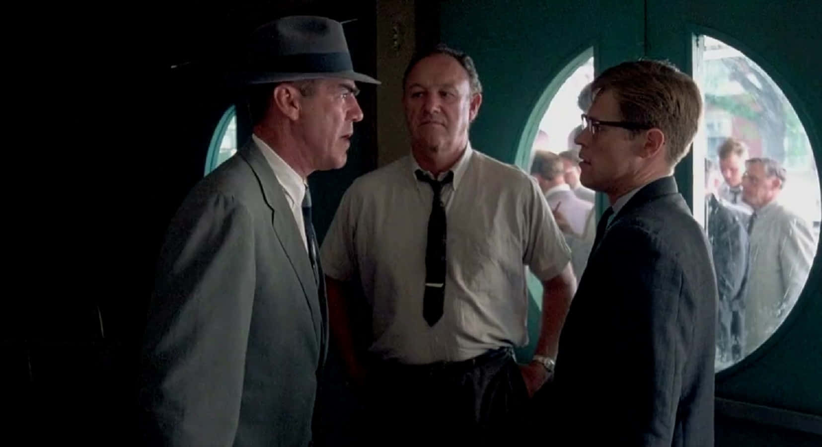 R. Lee Ermey 桌布 壁紙 — 三名身穿西裝、戴帽子的男子在燈光昏暗的火車車廂內激烈交談，圓形車窗外可見模糊的乘客。